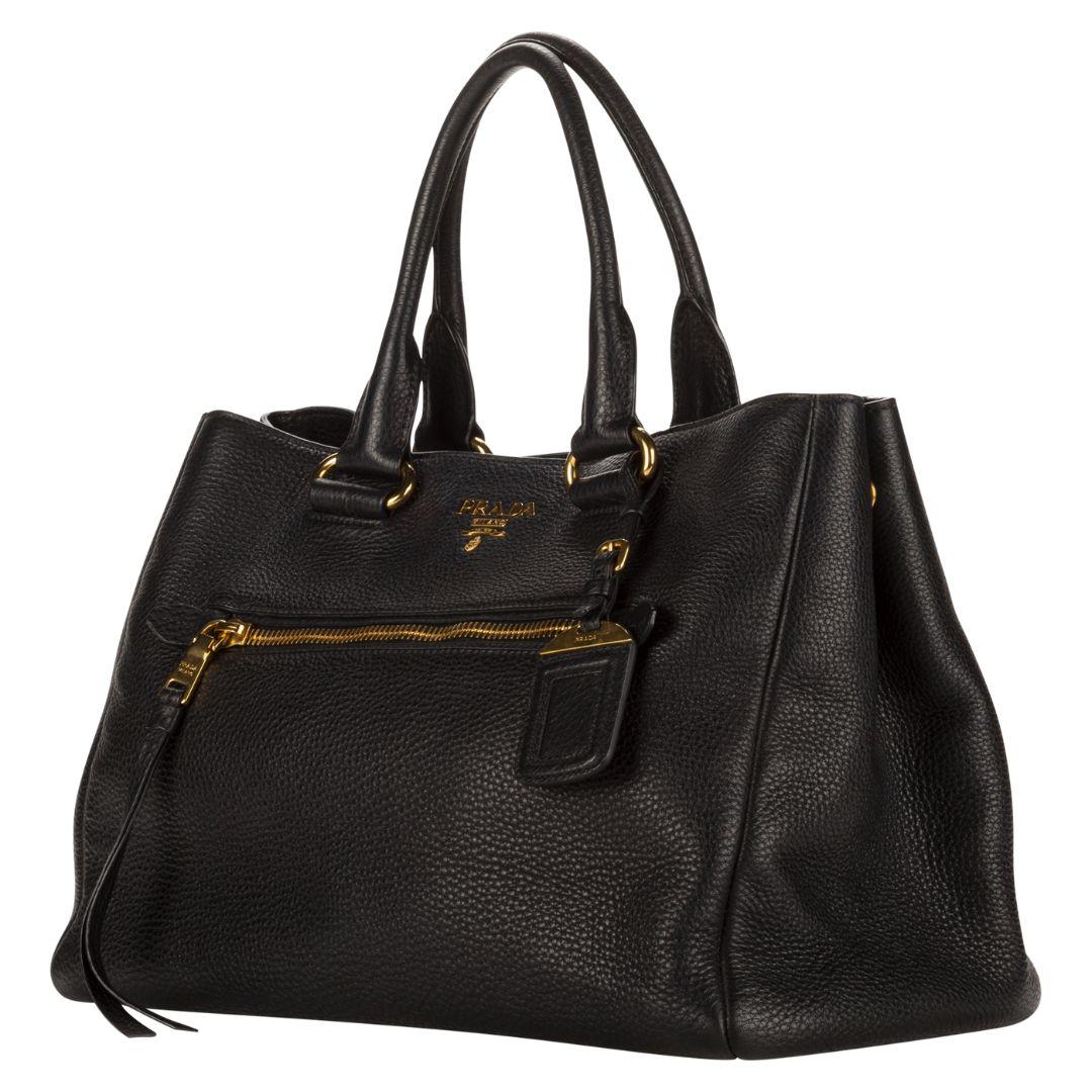 A sleek black calfskin leather tote from Prada, featuring luxurious gold-tone hardware. The magnetic snap closure opens to a logo jacquard interior, complete with a singular, practical interior pocket.

SPECIFICS
Length: 14.2