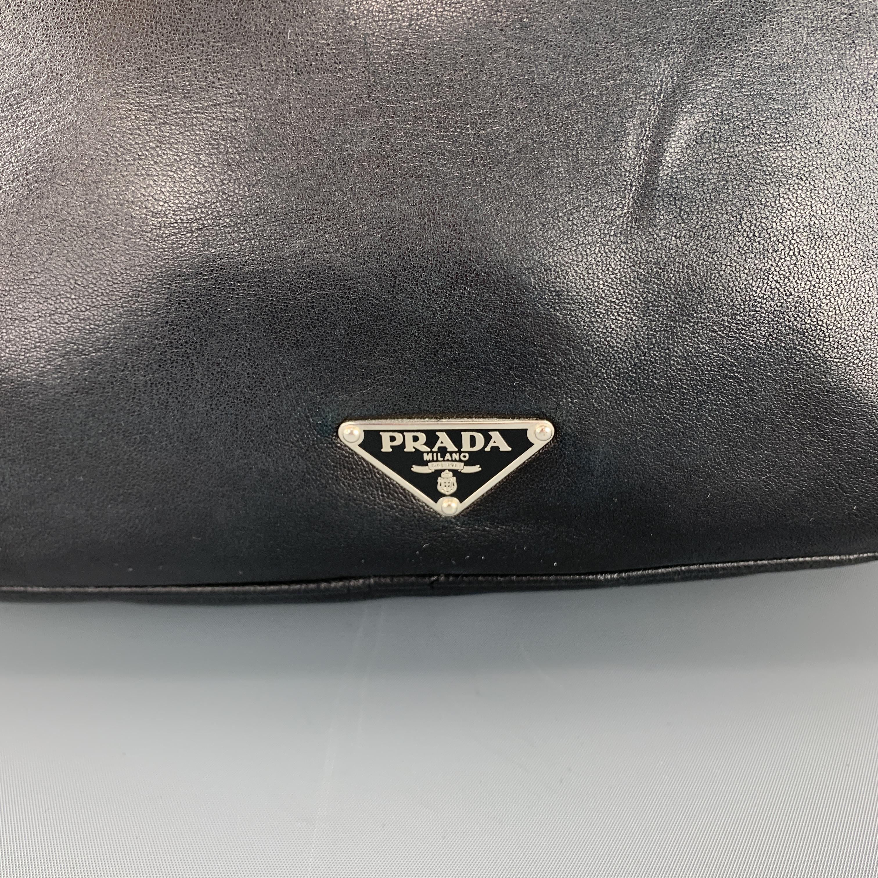 Vintage PRADA messenger bag comes in soft black leather with a frontal zip pocket, silver tone black enamel triangle plaque, back snap pocket, top zip closure, and webbing crossbody strap with leather accent. Wear throughout leather. As-is. Made in