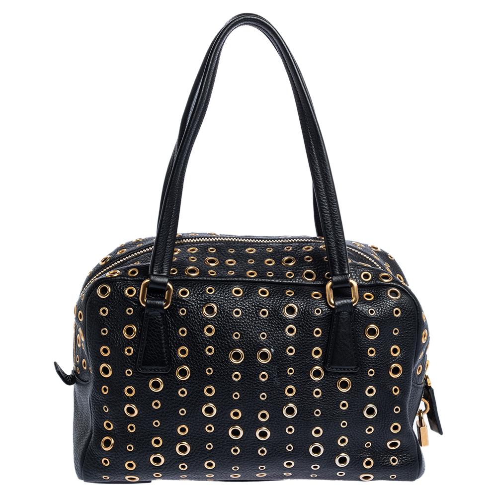 When you carry this Prada creation, be ready to catch admiring glances as this bag is stylish and handy. The bag has been crafted from leather in a lovely black shade and designed with gold-tone grommet embellishments all over as well as two top