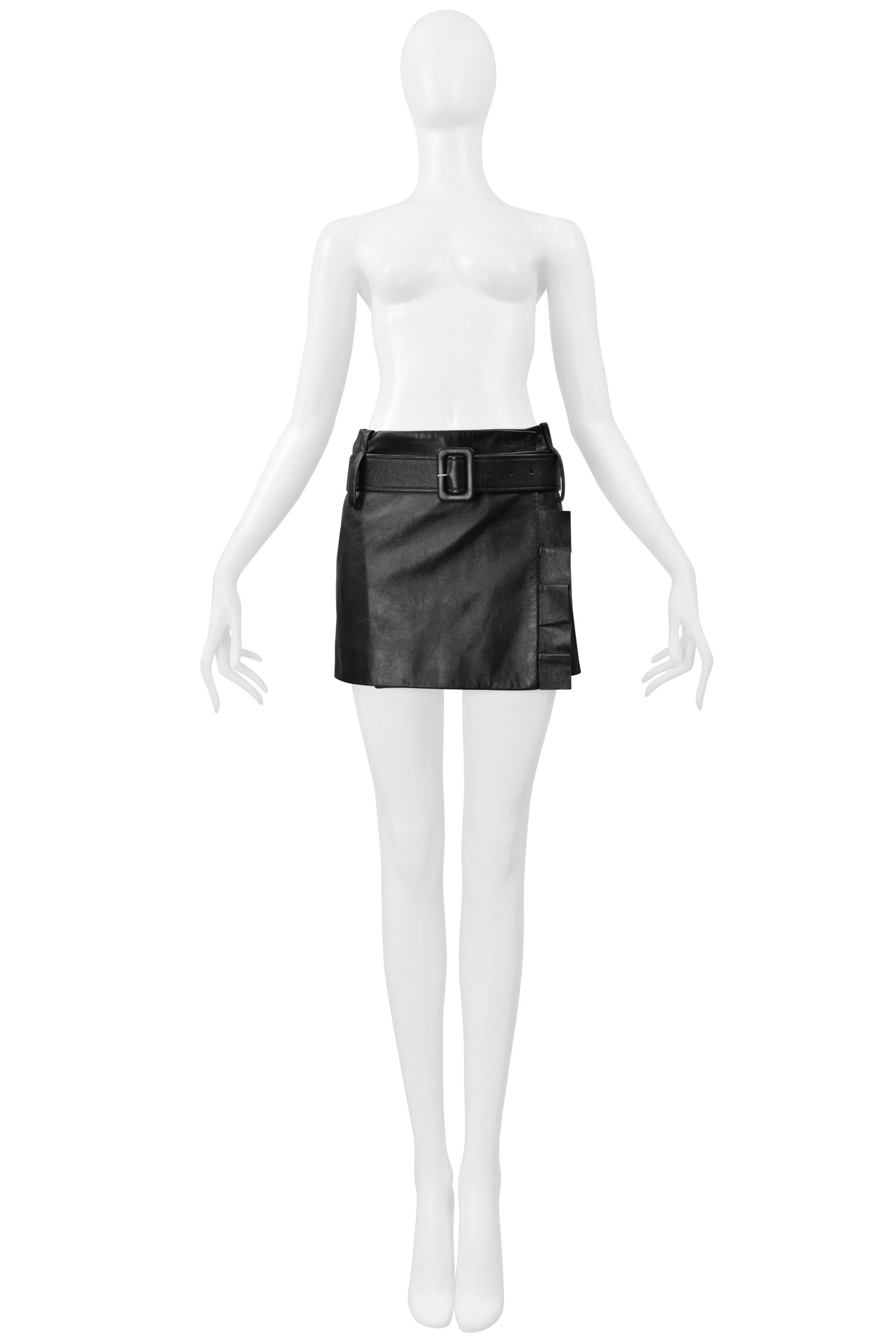 Resurrection Vintage is excited to offer a Prada black leather mini skirt with ruffles and a belt. The skirt features a wrapped effect, a removable and adjustable belt with a rectangular buckle, exaggerated belt loops, and pleated side