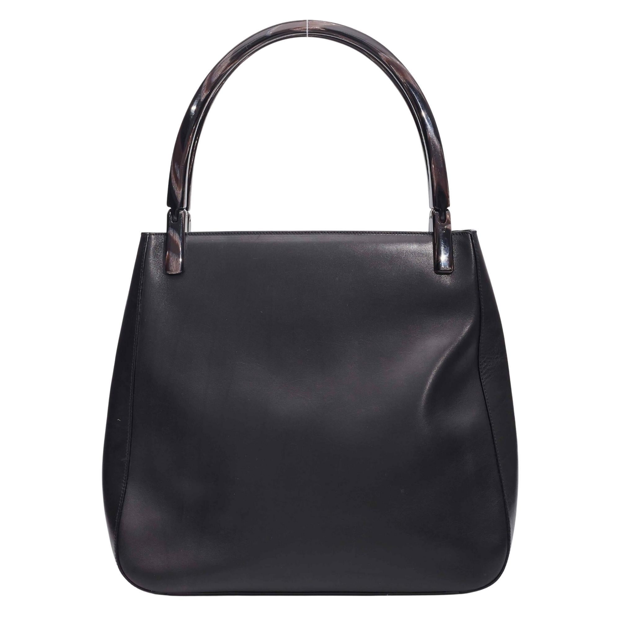 Prada Black Leather Acrylic Handle Tote. This tote from Prada features a leather construction, dual acrylic top handles, silver tone hardware and nylon logo lining.

Color: Black
Material: Leather
Code: 117
Measures: Height 11” x Length  12” x Depth