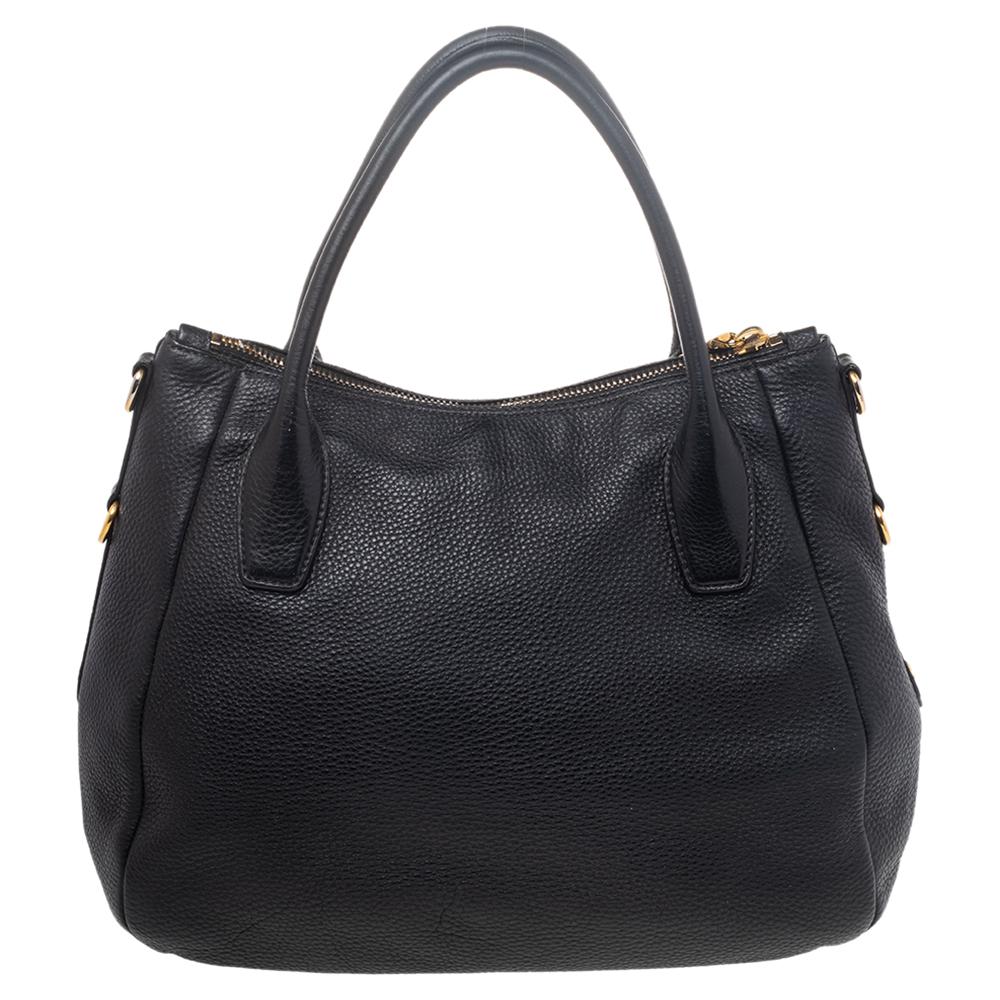 This Prada Sacca 2 Manici hobo is made of Vitello Daino leather. It features rolled top handles and gold-tone hardware. A recognizable Prada logo sits at the front. The interior is lined with durable nylon and comprises a slip pocket and enough