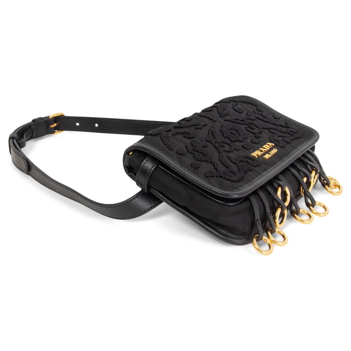 100% authentic Prada floral-embroidered Corsaire belt beg in black nylon with gold-tone metal O-ring fringe and calfskin trim. Removable and adjustable belt. Opens with a magnetic snap-flap closure to a black nylon logo lining with one slip pocket