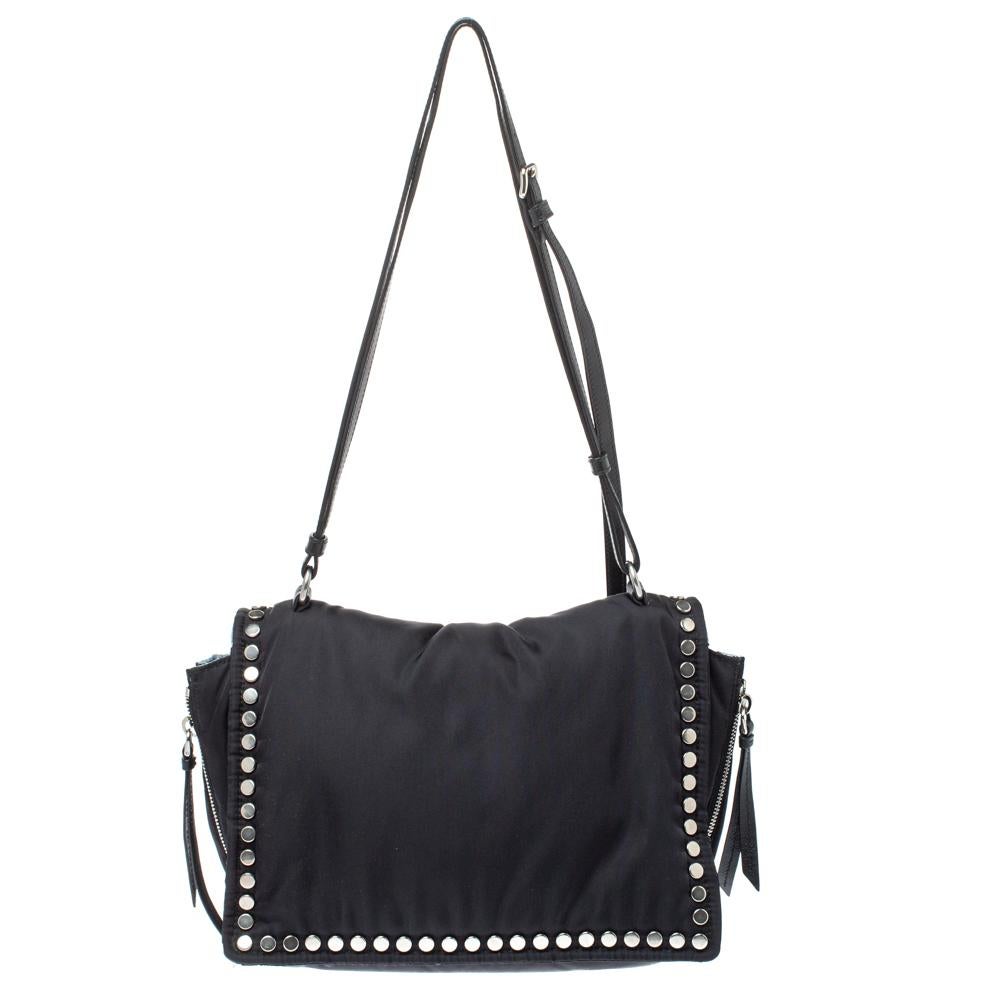 Die Etiquette Umhängetasche aus dem Hause Prada ist stilvoll und kantig. Sie wurde in Italien gefertigt und besteht aus Nylon und Leder. Diese schwarze Tasche hat silberfarbene Nieten und eine Frontklappe mit Logo, die sich zu einem geräumigen,