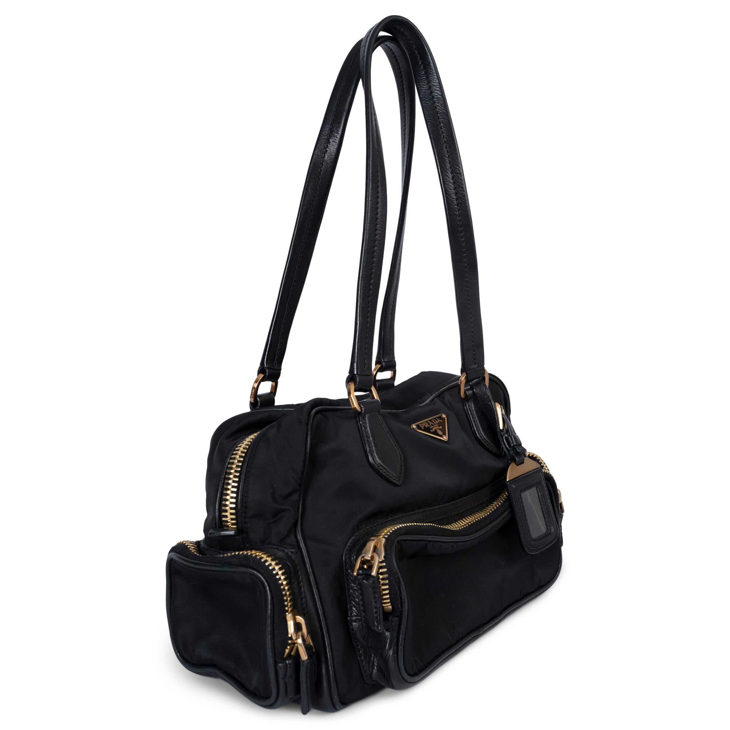 This 100% authentic Prada bowling bag is crafted from black nylon and features black leather trim, offering a sleek and functional design. It includes three zipper pockets and a flap pocket on the outside for easy access, along with a luggage tag