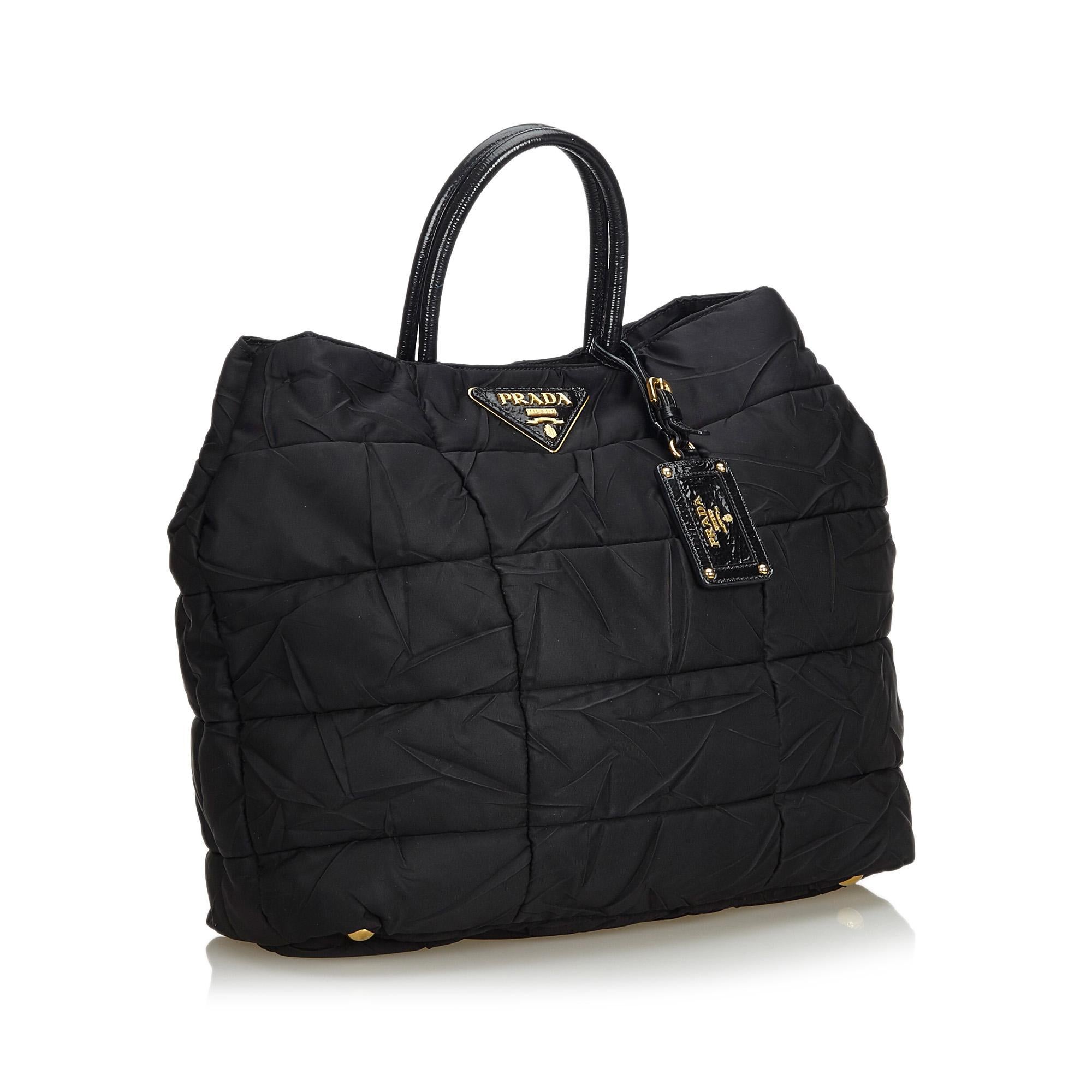 This tote bag features a quilted nylon body, rolled leather handles, an open top with a magnetic closure, and interior an interior zip pocket. It carries as B+ condition rating.

Inclusions: 
This item does not come with