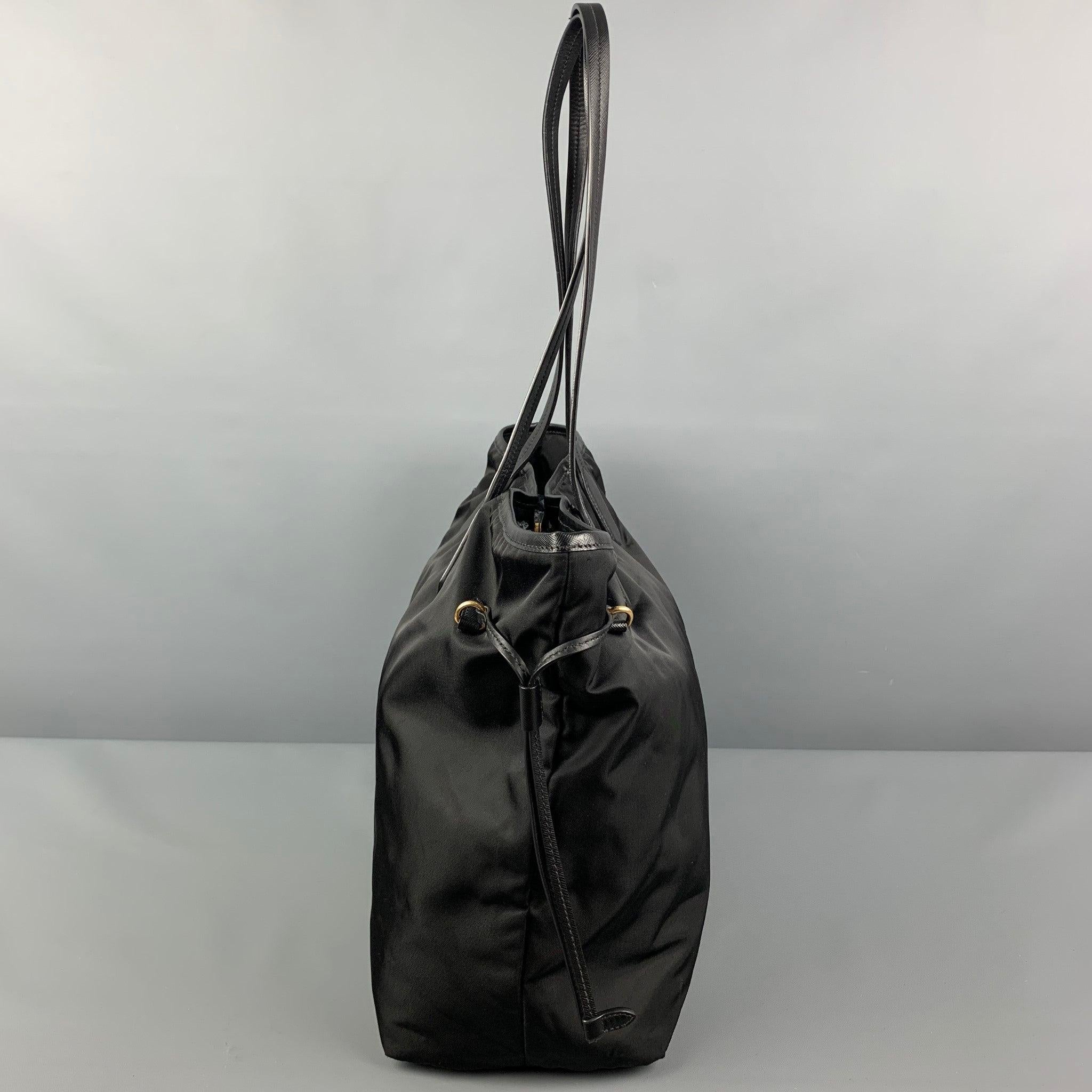 PRADA handbag comes in a black nylon featuring a tote style, leather trim, gold tone hardware, adjustable side straps, inner pocket, top handles, and a snap button closure. Made in Italy.
 Very Good
 Pre-Owned Condition. 
 

 Marked:  165 
 

