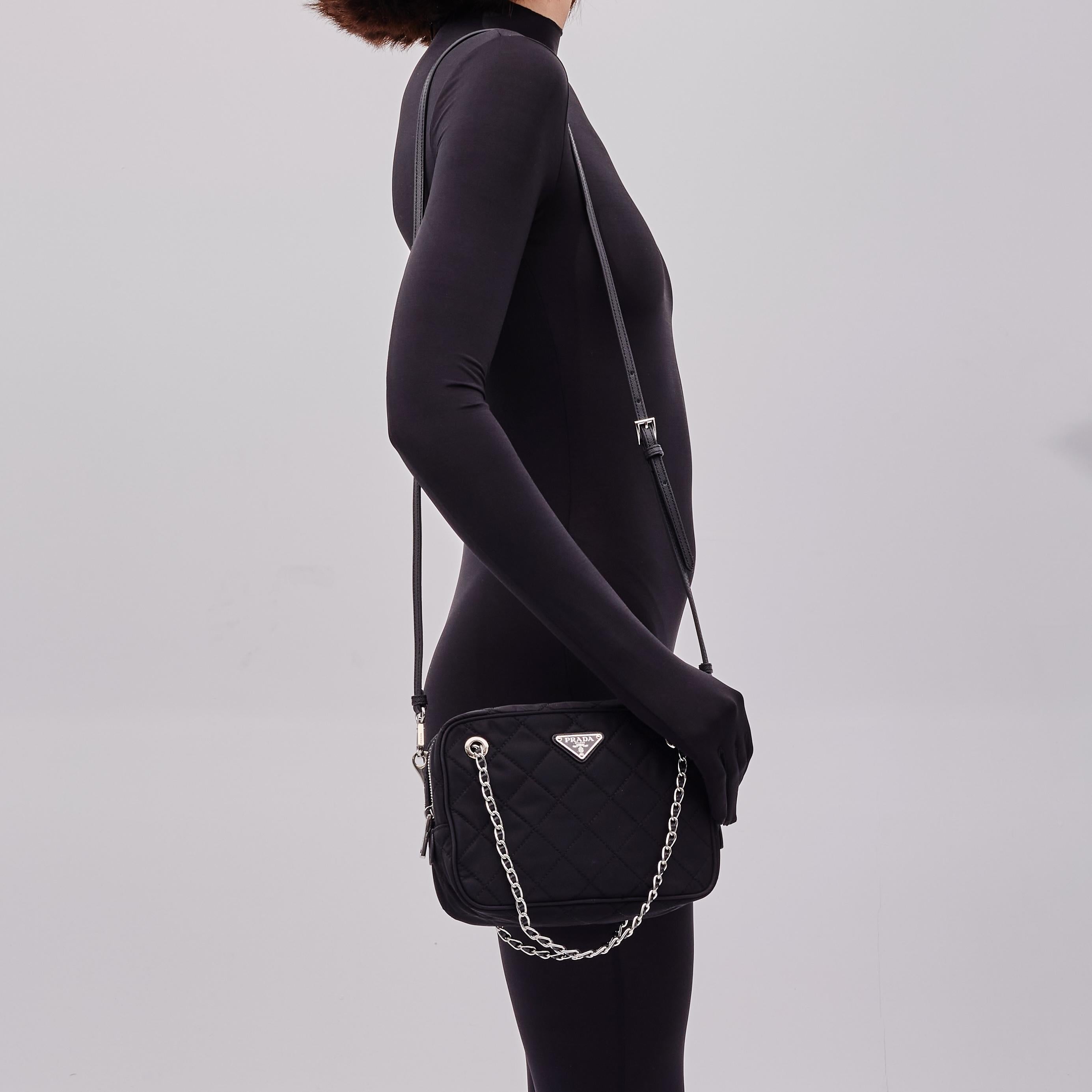 This shoulder bag is made of black quilted nylon and features a silver tone hardware, dual chain and leather shoulder strap, an optional leather strap, top zip closure and black  Outlet. 
Color: Black
Material: Nylon
Item code: 165
Comes with a dust