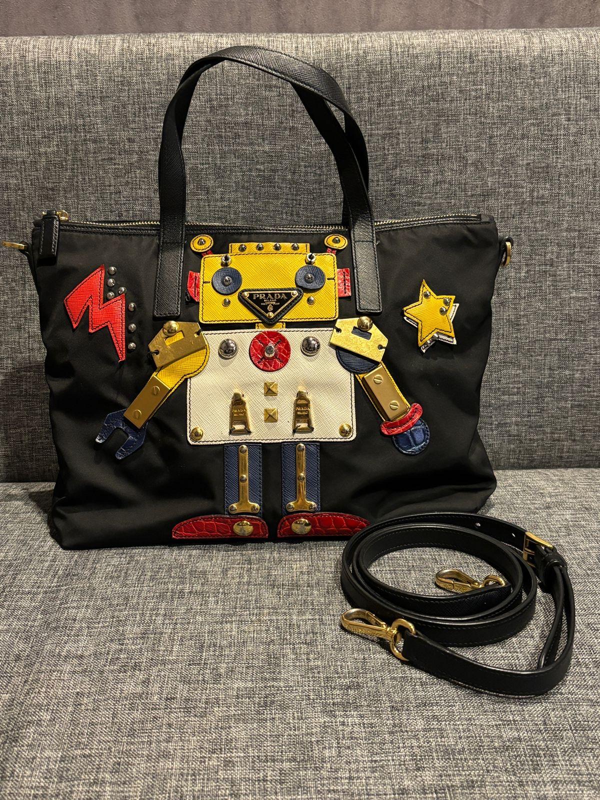Carinissima borsa tote robot di Prada in nylon. Viene fornito solo con il cinturino. Lievi segni sulla superficie in nylon. Alcune parti dell'abbellimento si sono appannate, ma non si notano troppo. 