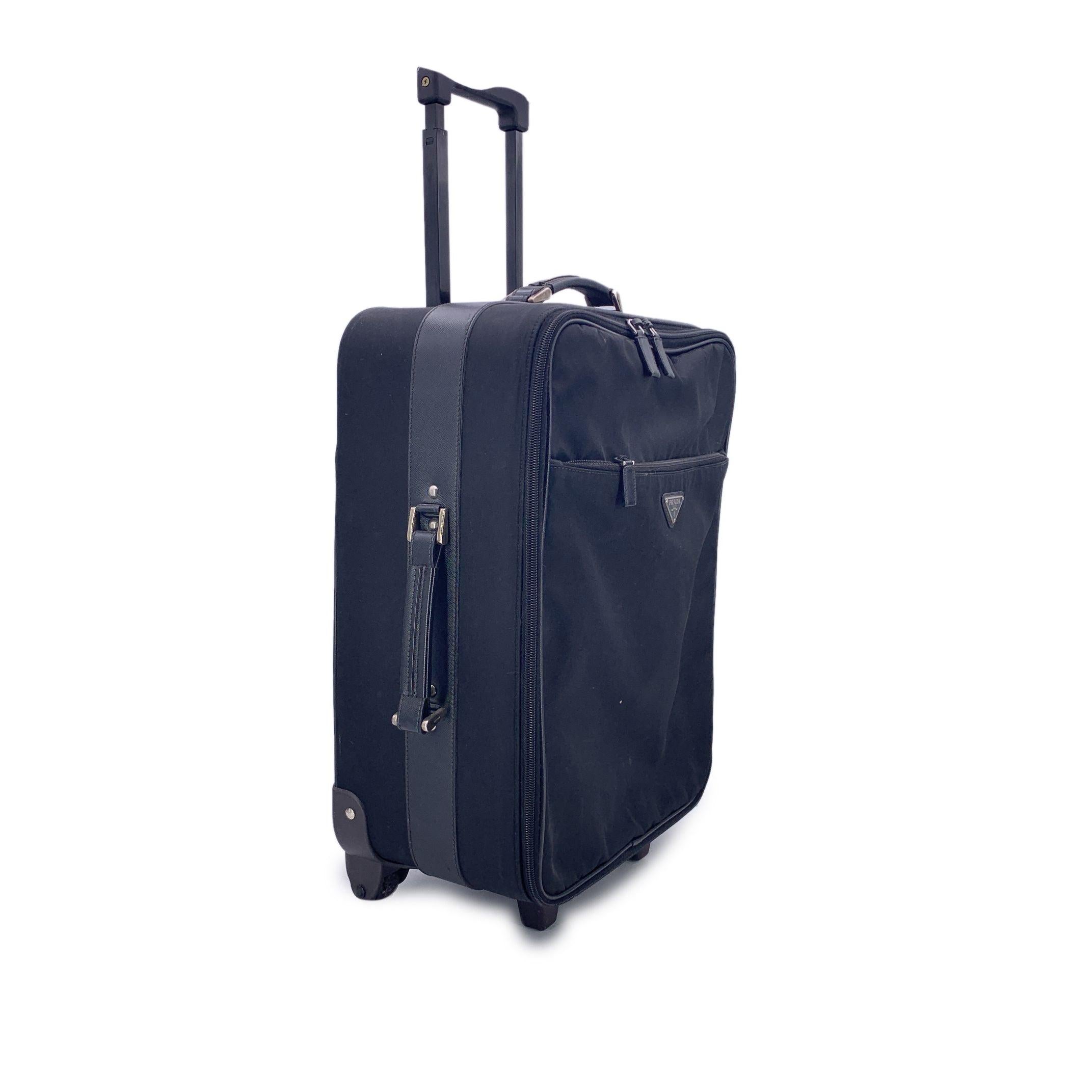 Reisen Sie in zeitlosem Stil mit dieser wunderschönen Prada Rolling Luggage Trolley Reisetasche, einem eleganten und funktionalen Begleiter für den anspruchsvollen Jetsetter. Dieses Modell aus strapazierfähigem schwarzem Nylon mit elegantem