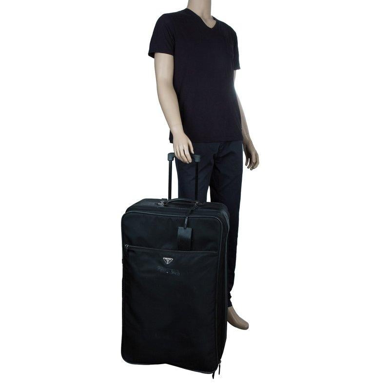 This signature rolling suitcase by Prada is an apt travel accessory with an elegant silhouette. It is made from black nylon and is accented with leather handles, trims, tag, and brand plaque. It features silver-tone hardware and a zipper pocket each