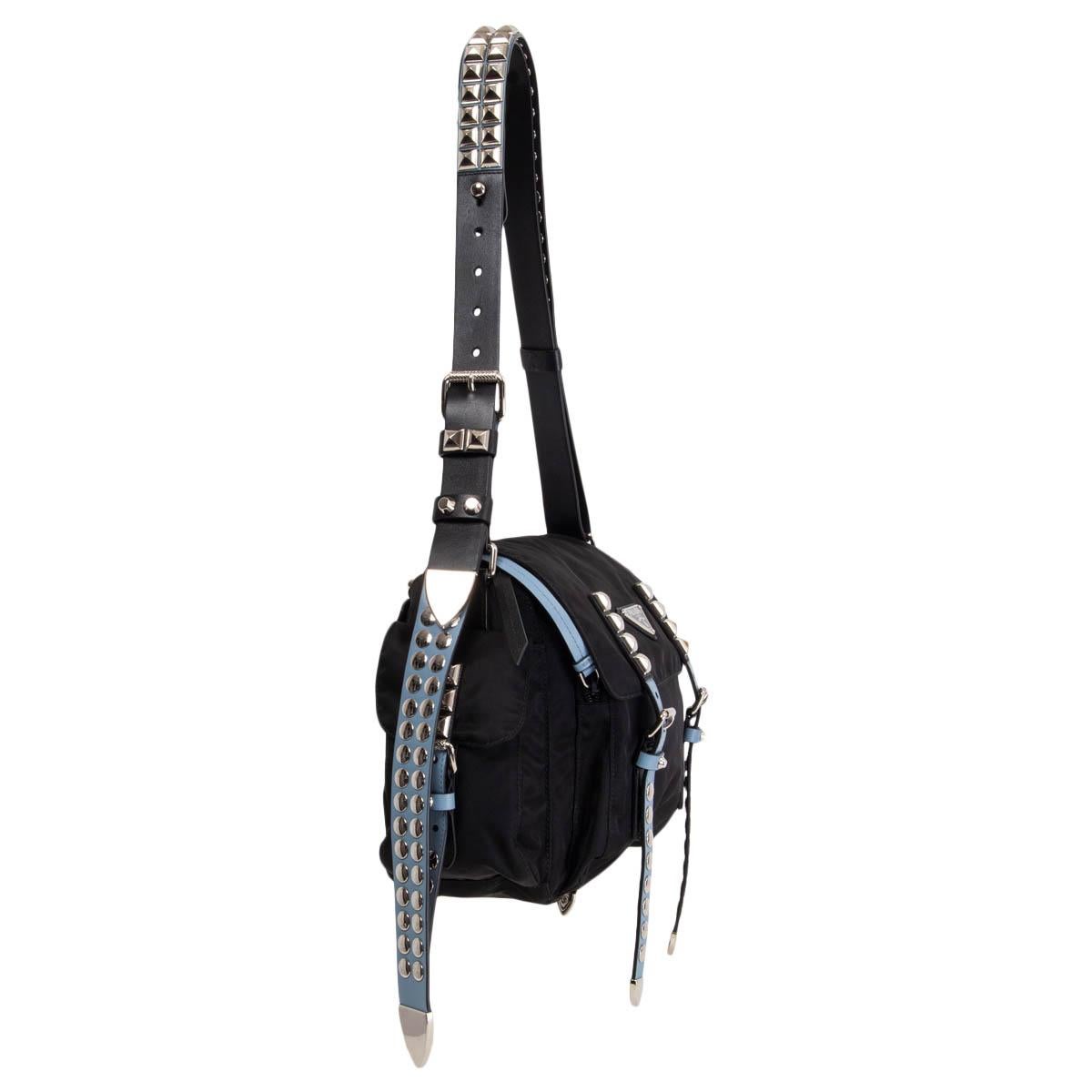 100% authentic Prada 'New Vela Studded' messenger bag in black nylon with black, Astrale (light blue) and white leather straps embellished with silver-tone studds. Opens with a zipper under the flap and is lined in classic black logo nylon with one