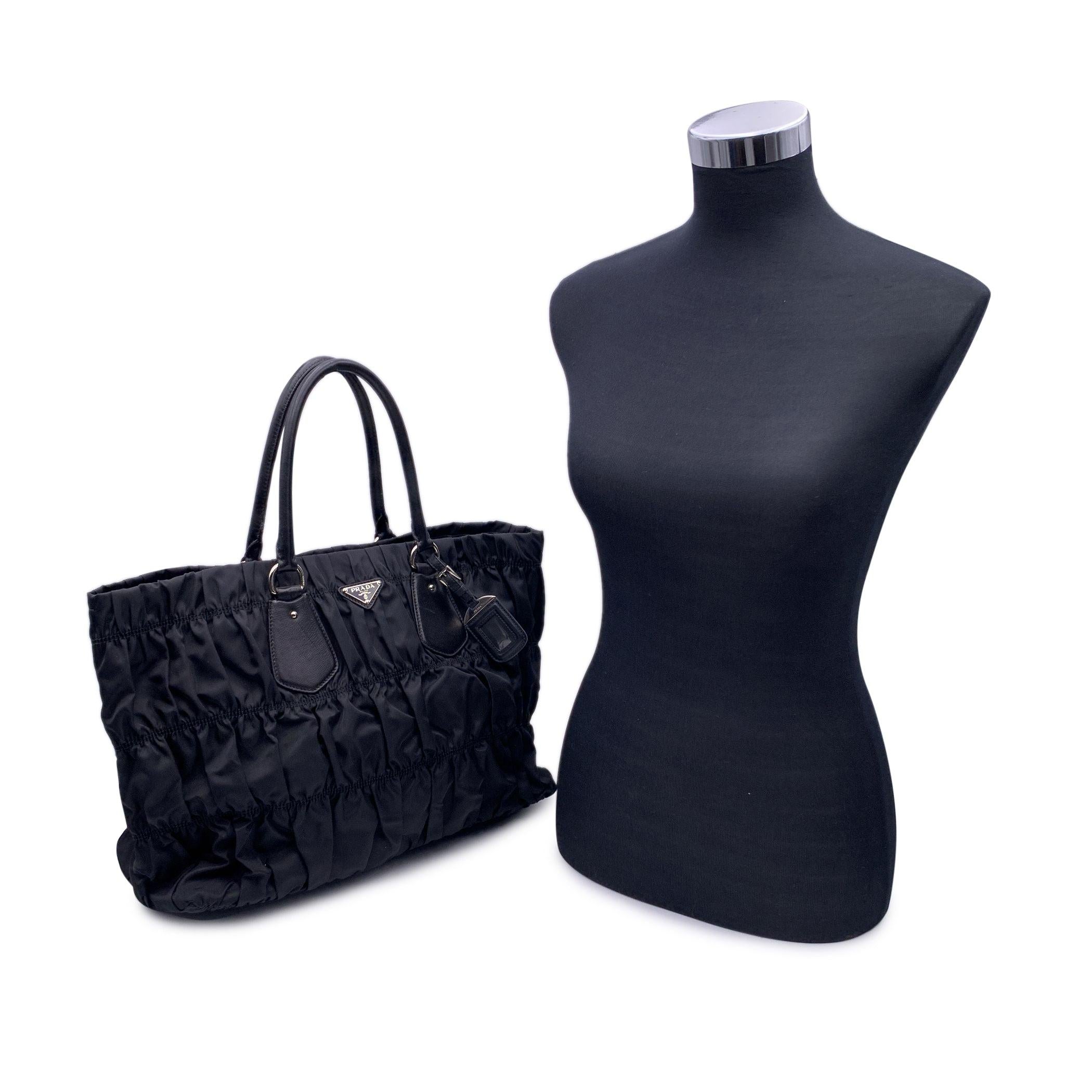 Elegant Prada Tessuto Gauffre Tote bag. The bag is crafted of black draped nylon with black leather trim, handles. ID tag with a clear window. Silver tone hardware. Prada triangle logo on the front. Upper magnetic button closure. Black lining. 1