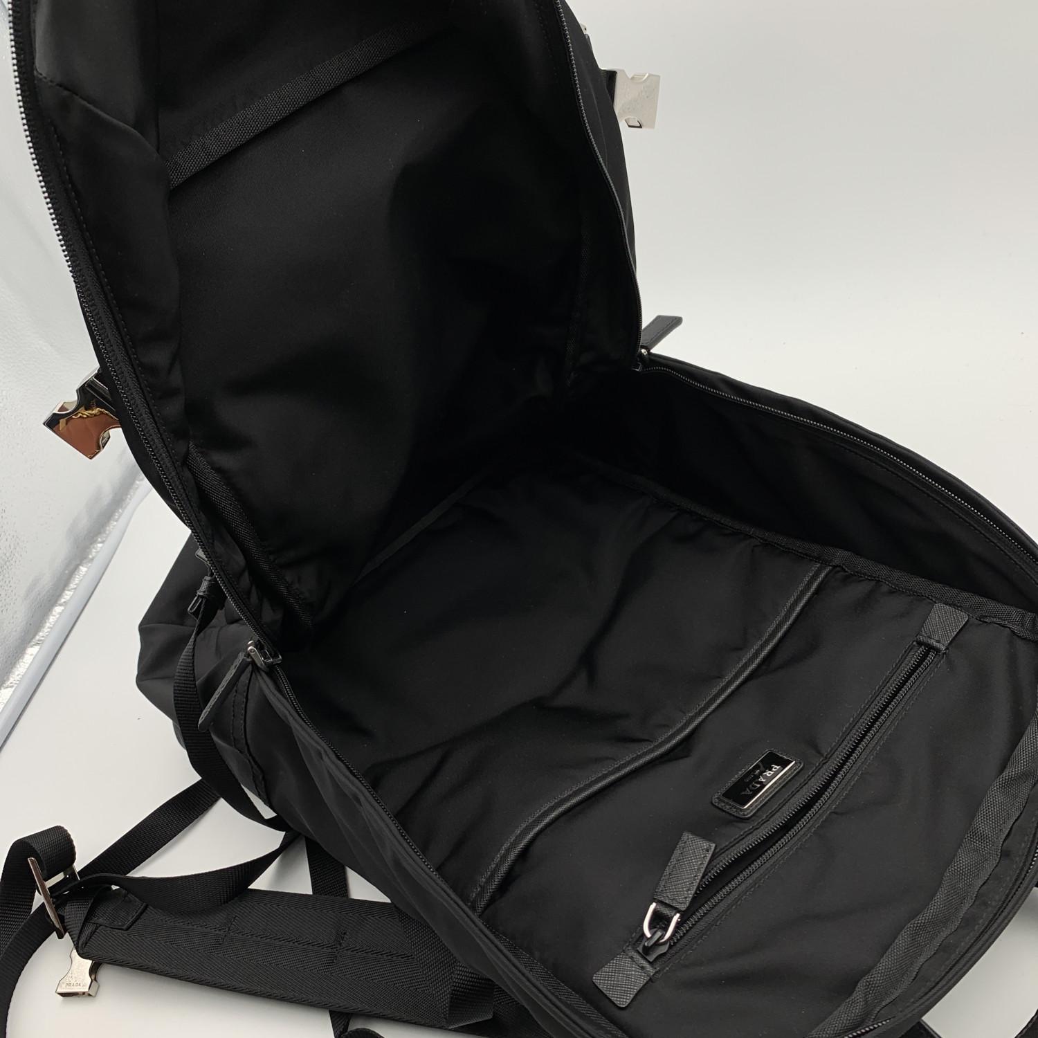 Mochila bandolera unisex Prada, mod. 2VZ022. Nylon negro con ribete saffiano negro y herrajes metálicos plateados. Correas acolchadas ajustables y espalda acolchada. Cierre superior de cremallera. Tres bolsillos exteriores con cremallera. Logotipo