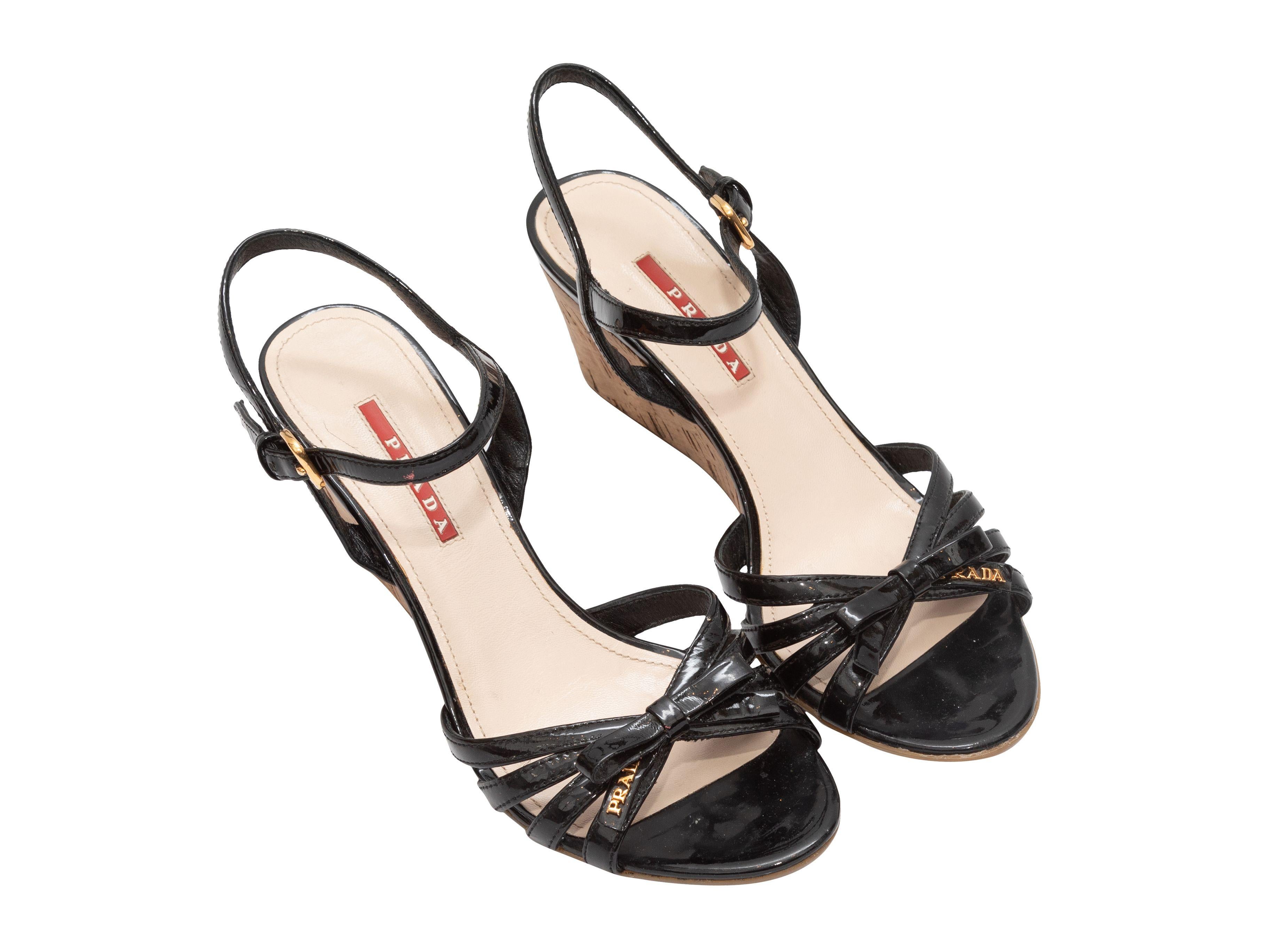 Product Details: Black patent leather bow wedge sandals by Prada. Gold-tone hardware. Cork soles. Buckle closures at ankle straps. 3