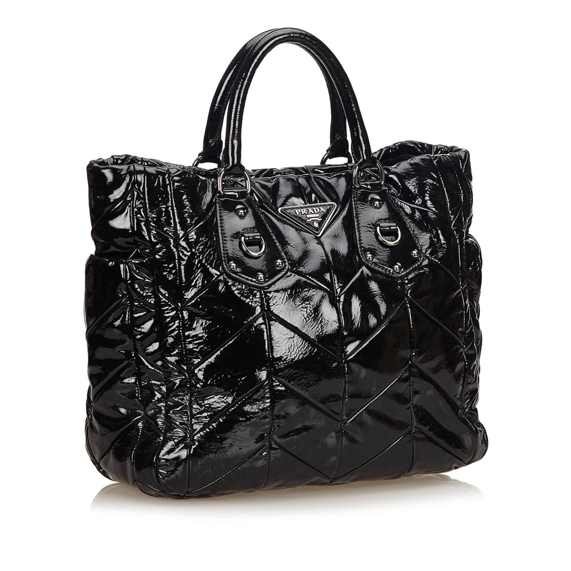 This tote bag features a patent leather body, rolled handles, open top, and interior zip and slip pockets. 

It carries a B condition rating.

Dimensions: 
Length 34 cm
Width 30 cm
Depth 11 cm
Drop 11 cm

Inclusions: Dust Bag, Shoulder Strap,