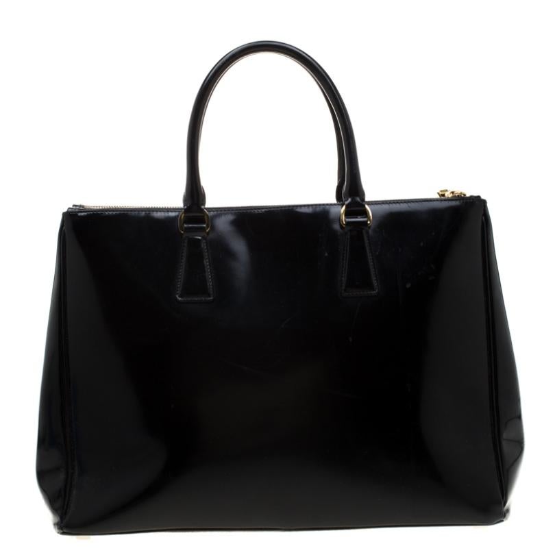 This elegant Spazzolato tote from Prada is crafted from patent leather and is perfect for daily use. The bag features double handles, a leather covered gold key ring, protective metal feet, and gold-tone hardware. It has a nylon lined interior that