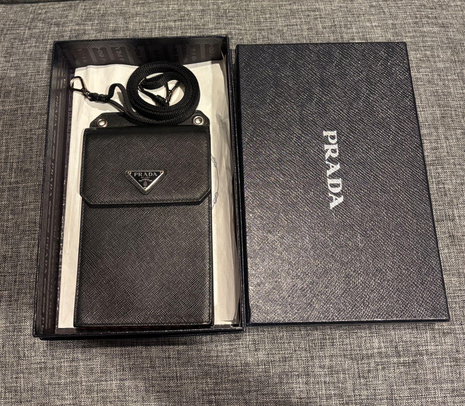 Porta telefono Prada in saffiano in ottime condizioni. Pelle nera con lati rossi. Lievi segni d'uso, solo lievi segni su alcune aree. Può essere indossato a spalla. Viene fornito con la sua scatola.