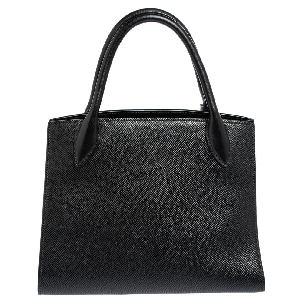 Diese Prada Monochrome-Tasche mit Metallschriftzug auf der Vorderseite steht für zeitlosen Luxus. Dieses Stück ist aus schwarzem Saffiano Cuir Leder gefertigt. Gleichzeitig akzentuieren goldfarbene Beschläge die Schönheit dieser Tragetasche. Zu