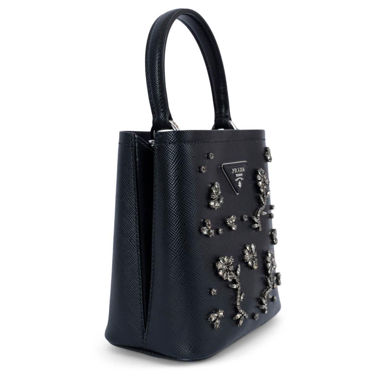 100% authentic Prada Crystal Panier Small Bucket Bag made of the iconic texture of black Saffiano leather embellished with crystal flowers and silver-tone hardware. The elegant design of the bag with single handle is distinguished for the magnetic