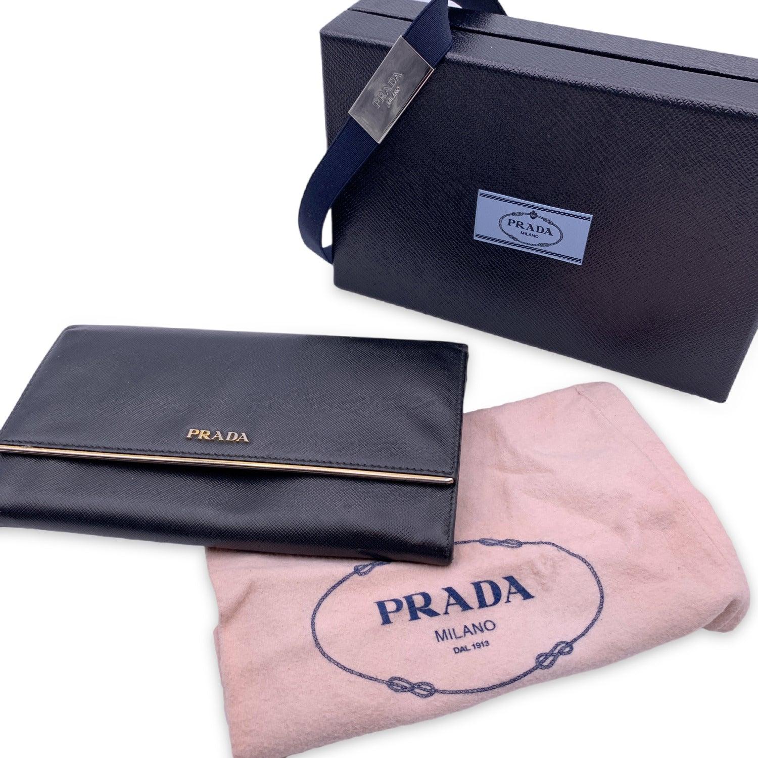 This beautiful Bag will come with a Certificate of Authenticity provided by Entrupy. The certificate will be provided at no further cost. Prada black Saffiano leather flap large wallet with gold metal bar detail and Pradalogo lettering. The snap