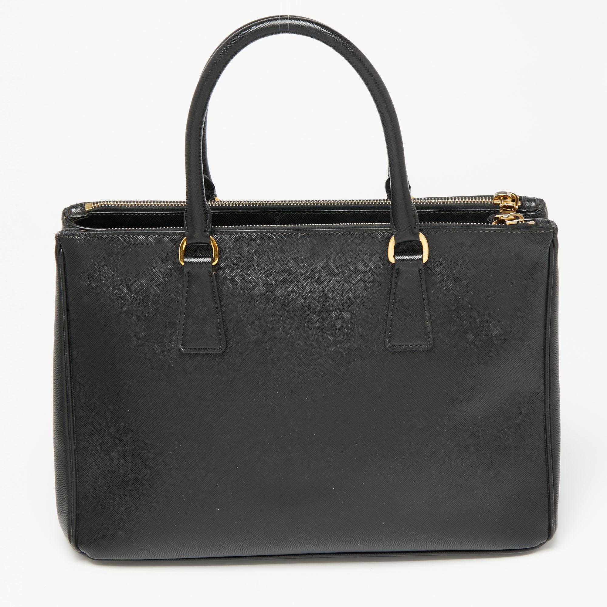Feminine in shape and grand in design, this Double Zip tote by Prada will be a loved addition to your closet. It has been crafted from Saffiano leather and styled minimally with gold tone hardware. It comes with two top handles, two zip