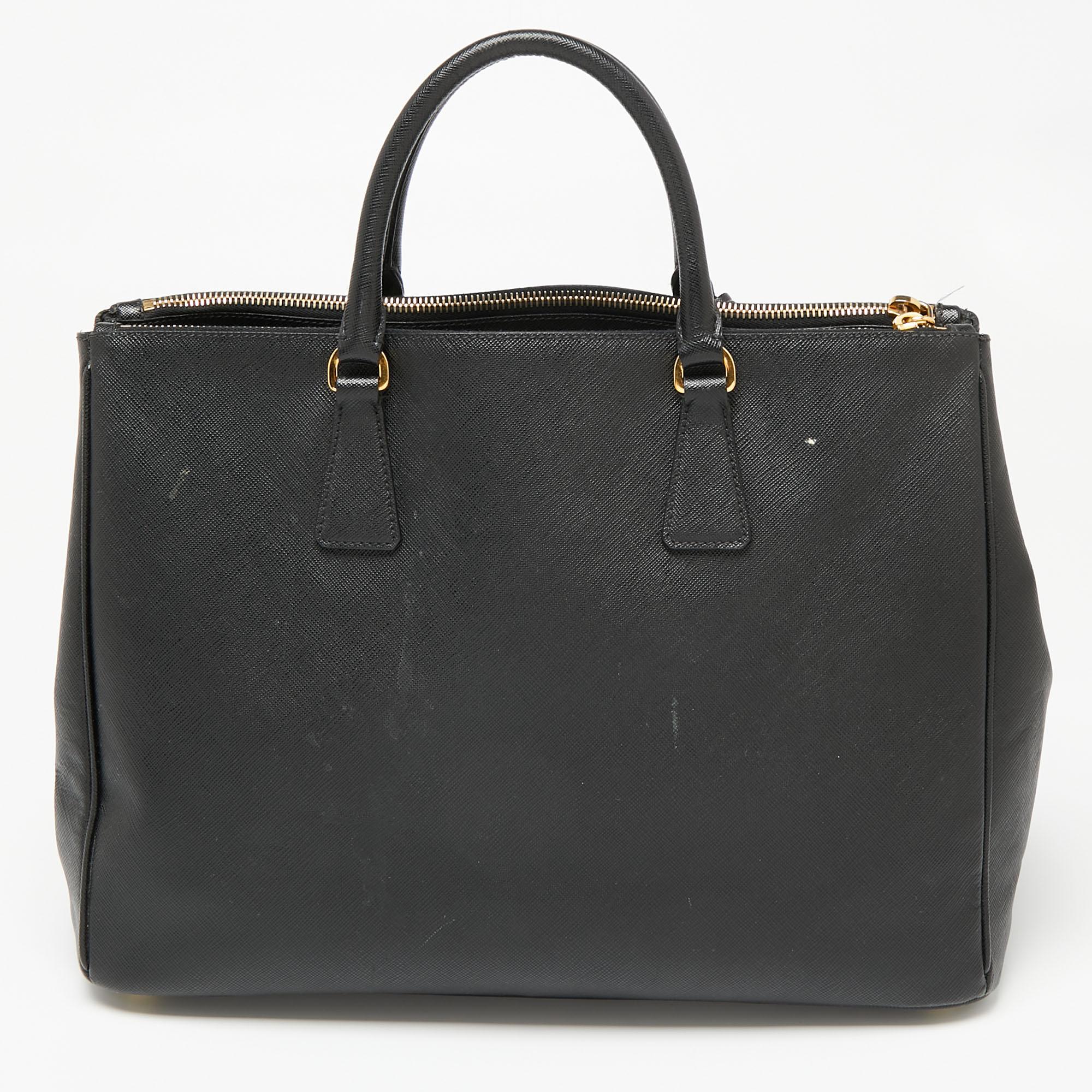 Loved for its classic appeal and functional design, Galleria is one of the most iconic bags from the house of Prada. This beauty in black is crafted from Saffiano leather and is equipped with two top handles, the brand logo at the front, and a lined