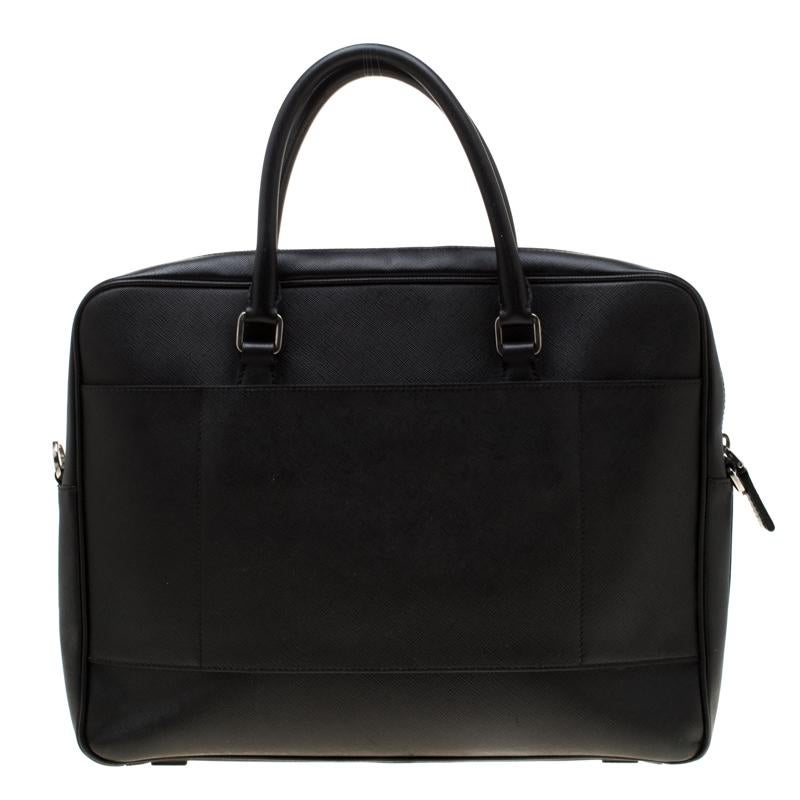 Finely crafted from Saffiano leather, this travel briefcase bag by Prada features a black shade along with two top handles and a leather tag attached to one of them. The top zipper opens up to reveal a nylon-lined interior that is perfectly sized to