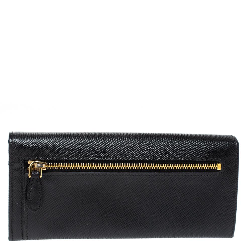 Dieses schwarze Portemonnaie von Prada ist aus Saffiano Lux Leder gefertigt und hat einen schönen Stil. Sie ist mit einer Klappe versehen:: die ein Innenleben mit Fächern und einem Reißverschlussfach offenbart. Die Schleife auf der Vorderseite trägt