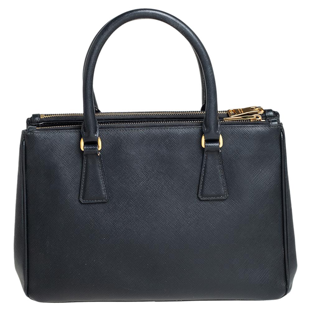 Loved for its classic appeal and functional design, Galleria is one of the most iconic and popular bags from the house of Prada. This beauty in black is crafted from Saffiano Lux leather and is equipped with two top handles, the brand logo at the