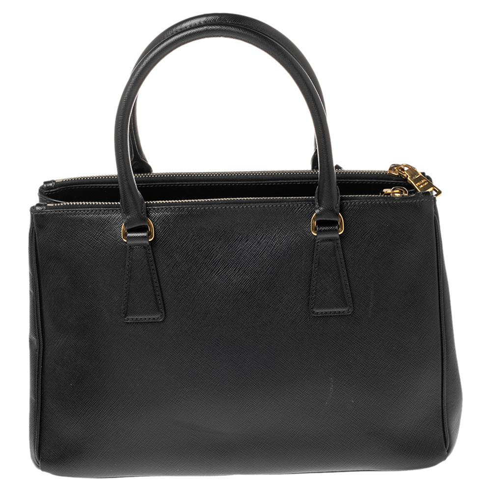 Loved for its classic appeal and functional design, Galleria is one of the most iconic and popular bags from the house of Prada. This beauty in black is crafted from Saffiano Lux leather and is equipped with two top handles, the brand logo at the