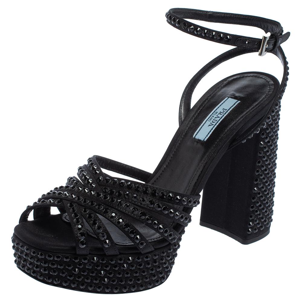 Be ready to catch the light whenever you step out in this pair of black sandals by Prada. They are covered in crystals on the upper cross straps, ankle fastening, platforms, and block heels. Add the sandals to your collection today and get set to