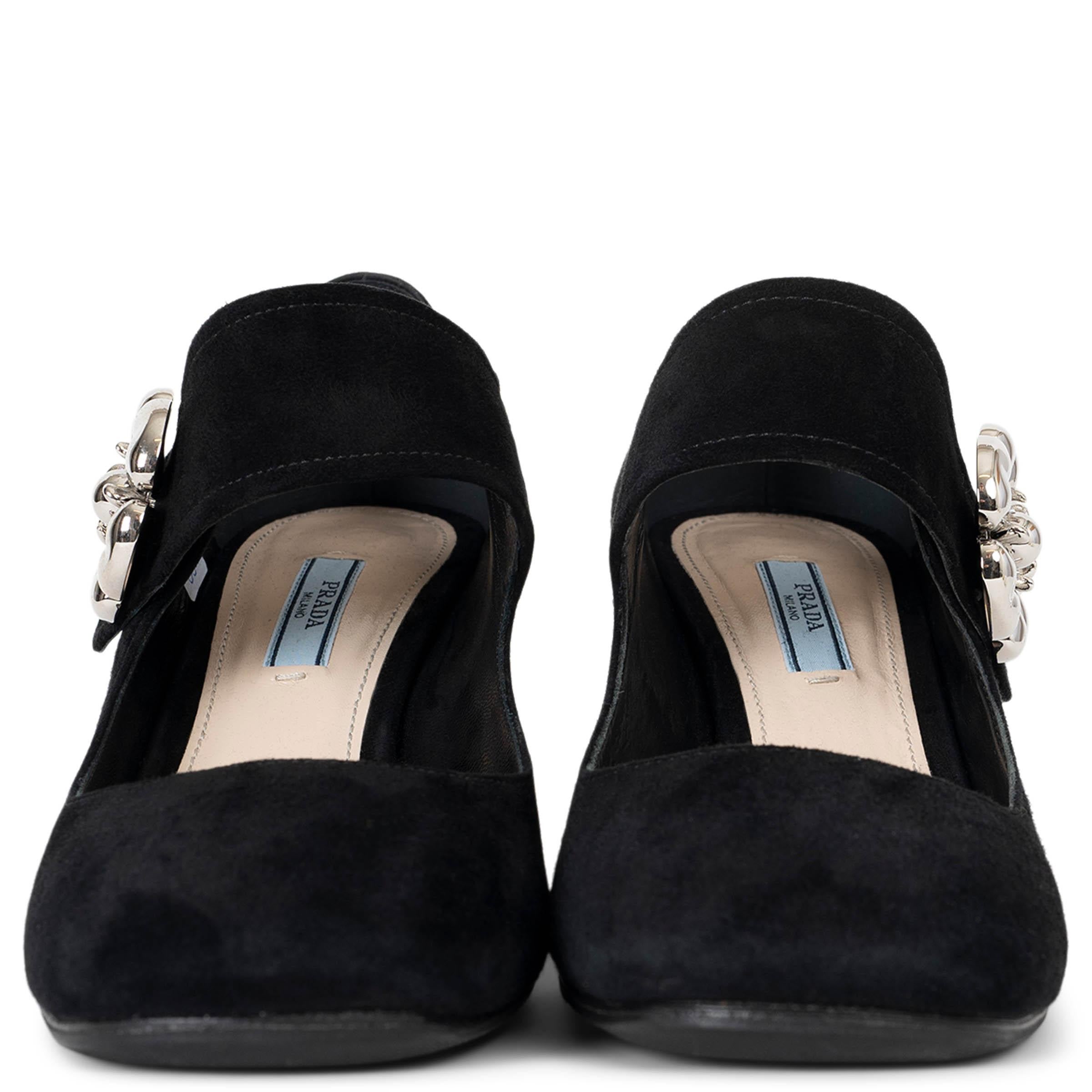Estos zapatos de salón Prada 100% auténticos están fabricados en lujoso ante negro, con una clásica punta redonda y un llamativo adorno de flor metálica plateada en el lateral. Diseñados con un cómodo tacón redondo en bloque, estos zapatos de salón