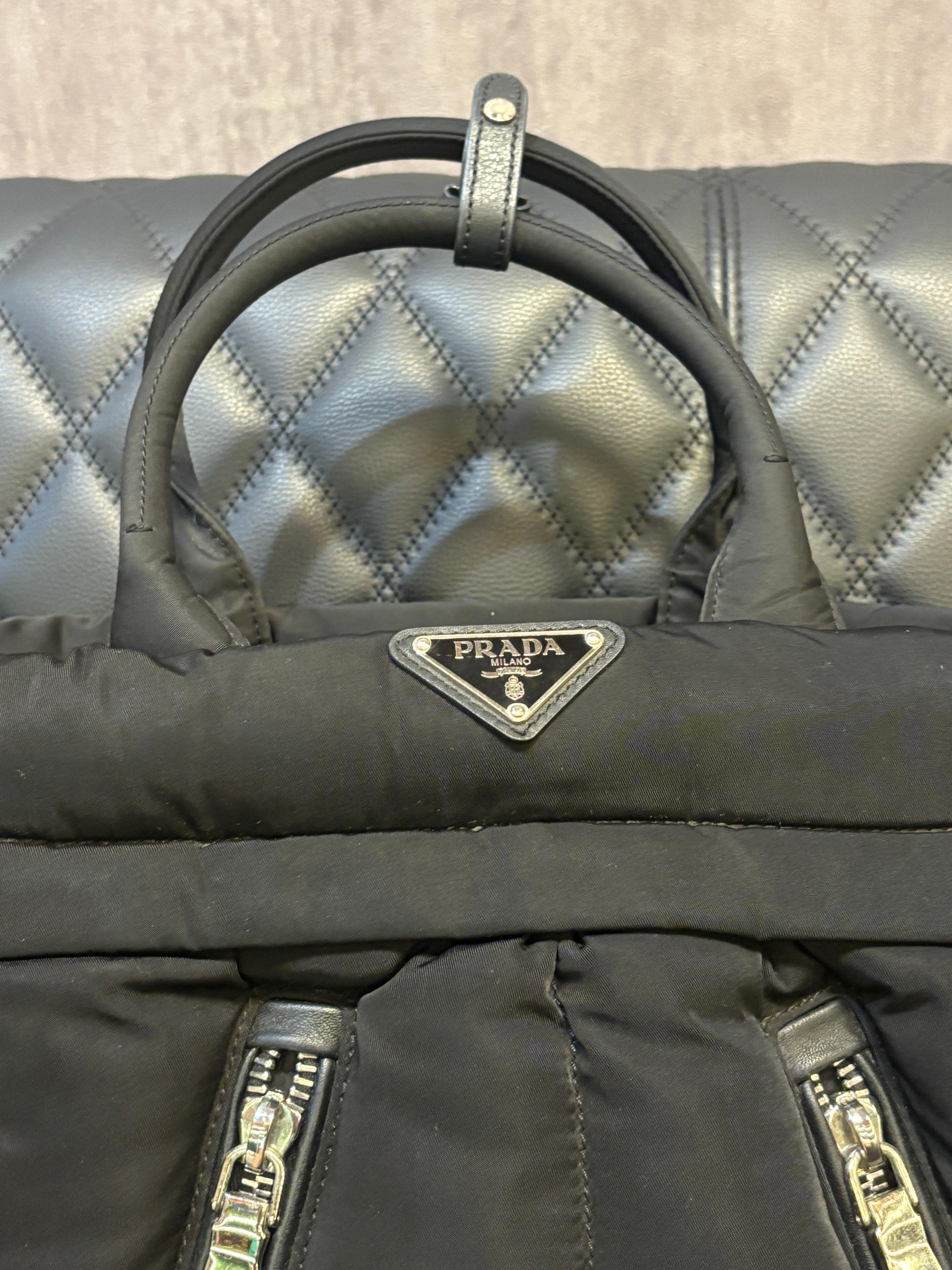 Tote bomber grande di Prada in nylon nero. Facile da indossare e dal design unico. Piccoli segni e graffi sulla superficie della Fabrice. Viene fornito con manico in pelle, tracolla rimovibile, etichetta e sacchetto antipolvere.