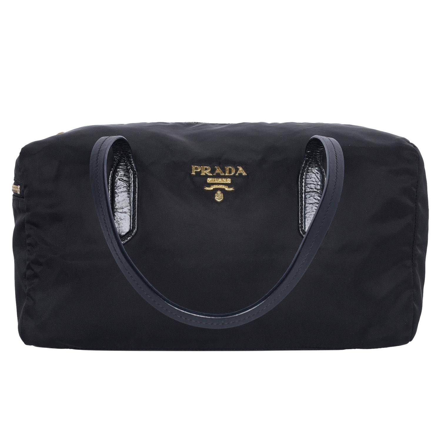 Authentic, pre-loved Prada Tessuto black nylon duffle shoulder bag. This bag features a nylon body, zipper top closure, side zipper pocket, gold Prada decal on the front, leather shoulder straps, gold hardware and large interior with a zipper slip