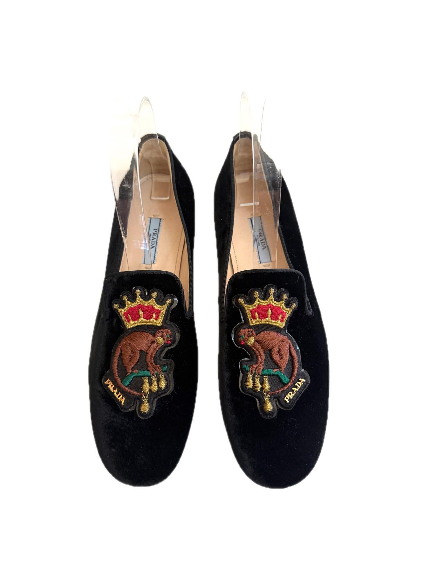 Prada Mocassini in velluto nero con stemma ricamato, Autunno/Inverno 2016, misura 37,5

Squisiti mocassini Prada realizzati in velluto nero felpato con un sorprendente motivo a cresta ricamato con il disegno di una scimmia coronata. Dalla collezione