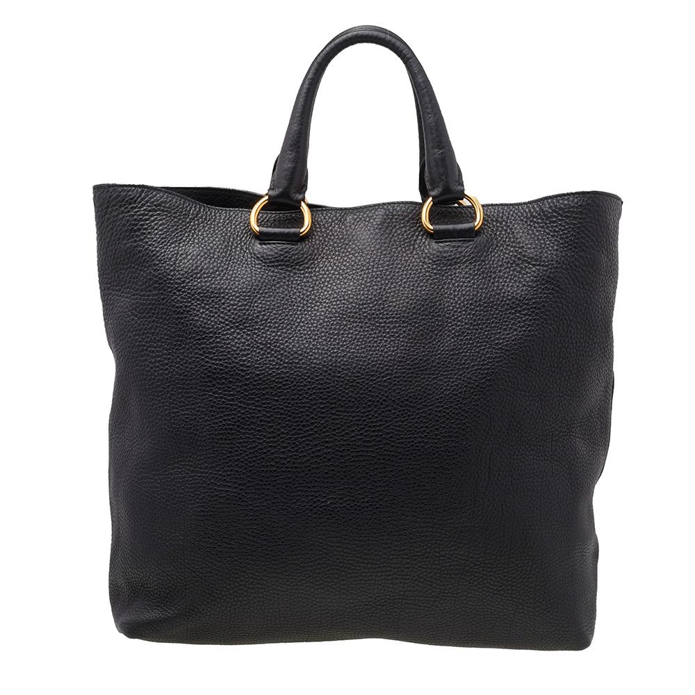 In a versatile shade and classic shape, this Vitello Daino Shopping tote by Prada is timeless. Crafted from supple black leather, the exterior is accented with a Prada label, leather ID tag, leather handles, and a removable flat shoulder strap.