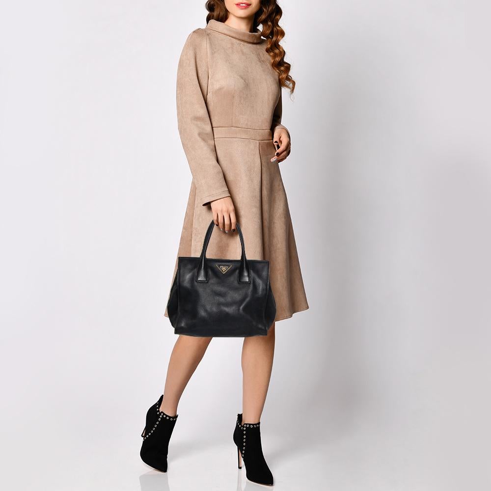 Unglaublich stilvoll und hochfunktional - diese Prada-Tasche ist der perfekte Begleiter für Ihre täglichen Besorgungen! Sie ist aus schwarzem Vitello Daino-Leder gefertigt und mit seitlichen Druckknöpfen und dem Markenlogo auf der Vorderseite