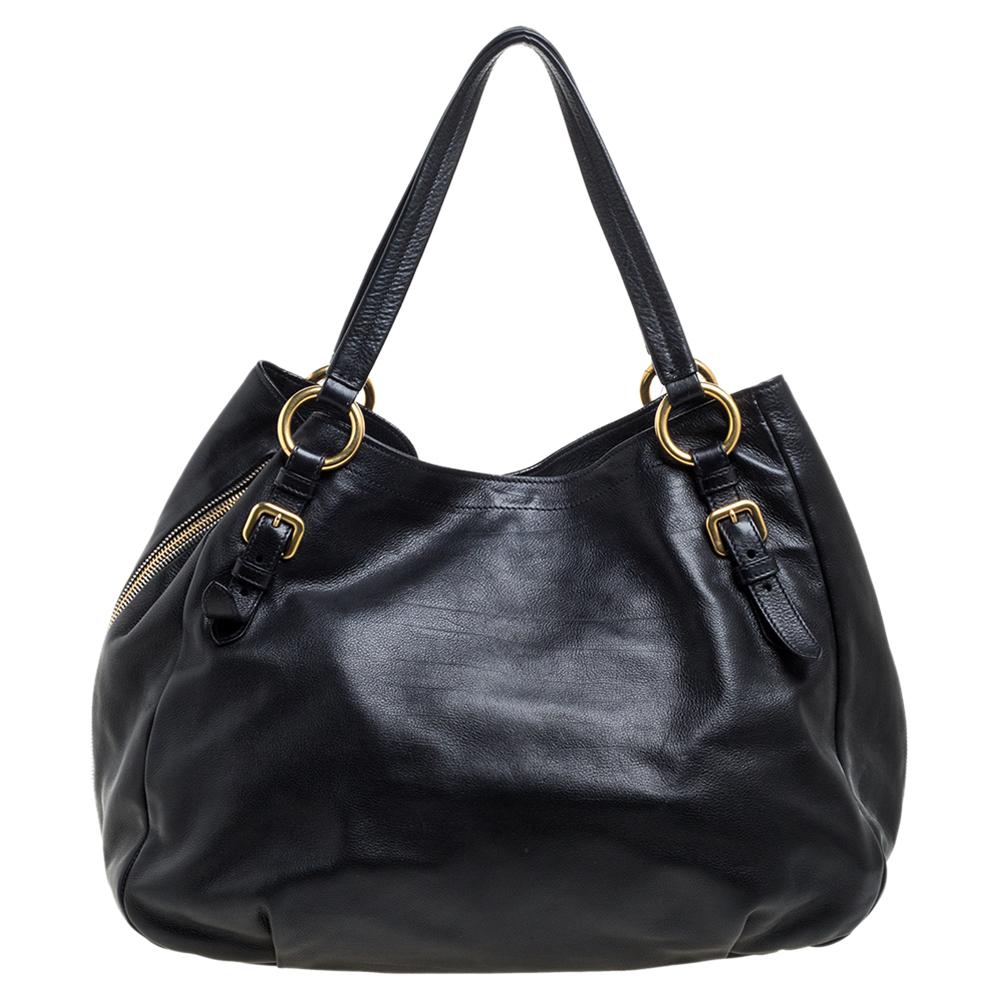 This Prada Sacca 2 Manici tote is made of Vitello leather. It features rolled top handles and gold-tone hardware. A recognizable Prada logo sits at the front. The interior is lined with durable nylon and comprises of a zip pocket and enough space