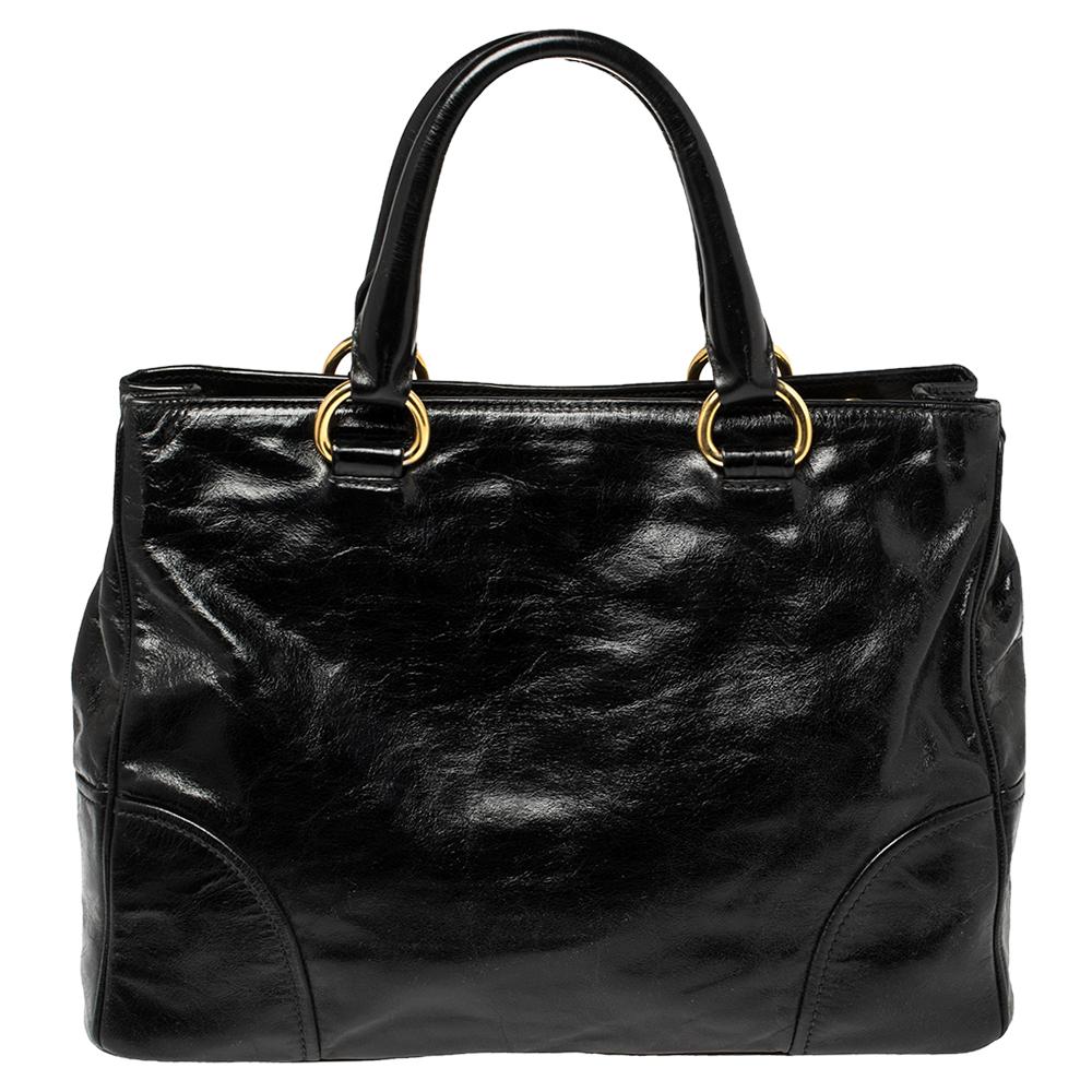 This Vitello Shine leather bag by Prada is artistically designed to reflect your style and add ease to your daily life. The black tote for women is equipped with two handles and nylon compartments, and complemented by gold-tone hardware. Complete