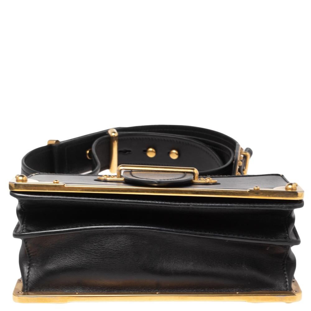 Inspired by valuable books from ancient times, the Cahier by Prada is a best-seller. This bag is crafted in Italy with black & white leather. It features a gold-tone loop at the front that adds a touch of contrast. The strap closure with the brand