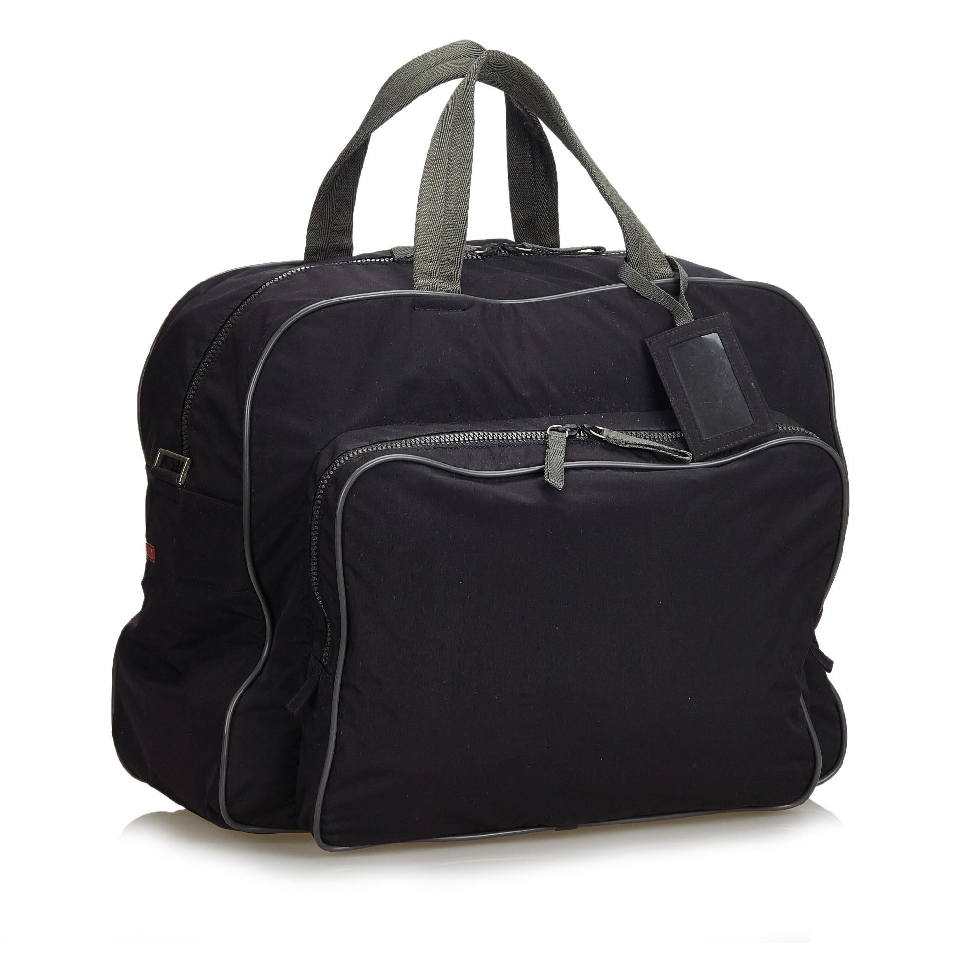 This duffle bag features a fabric body with leather trim, a front exterior zip compartment, flat handles with a luggage tag, a detachable flat strap, a top zip closure and interior zip and slip pockets. It carries as AB condition