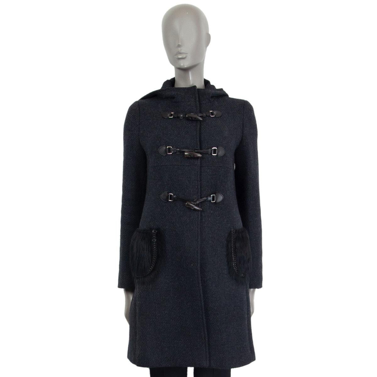 Prada duffle coat in dark grey virgin wool (100%) with a hood and black sheep fur pockets with braided metal trim details. Closes on the front with three wood horn shaped toggles and snap buttons. Lined in viscose (assumed as content is missing from