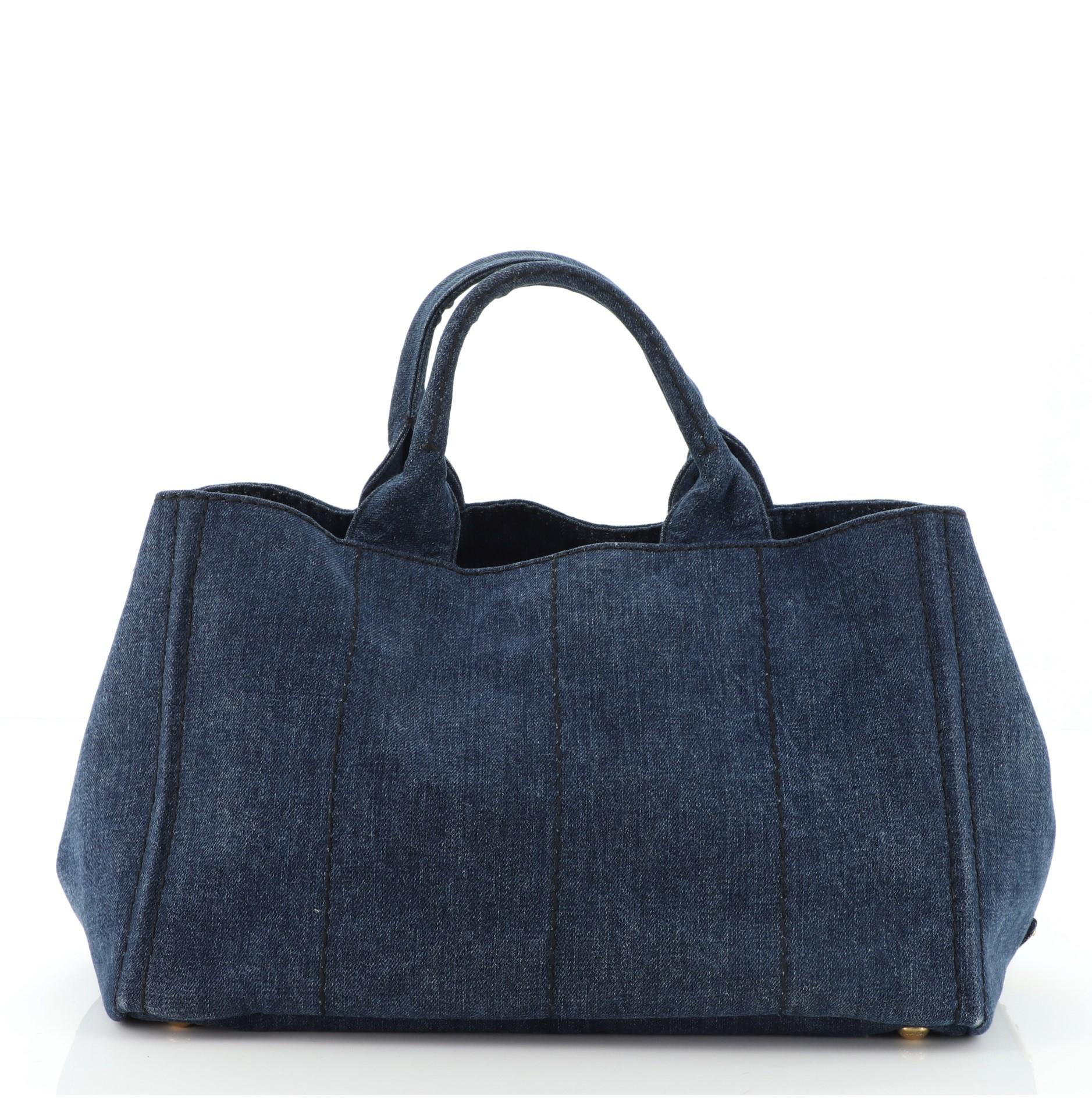 Prada Canapa Convertible Tote Denim Medium is crafted in blue denim and canvas, features dual top handles, side snap buttons, protective base studs, and gold-tone hardware. It opens to a blue denim and canvas interior with side zip and slip