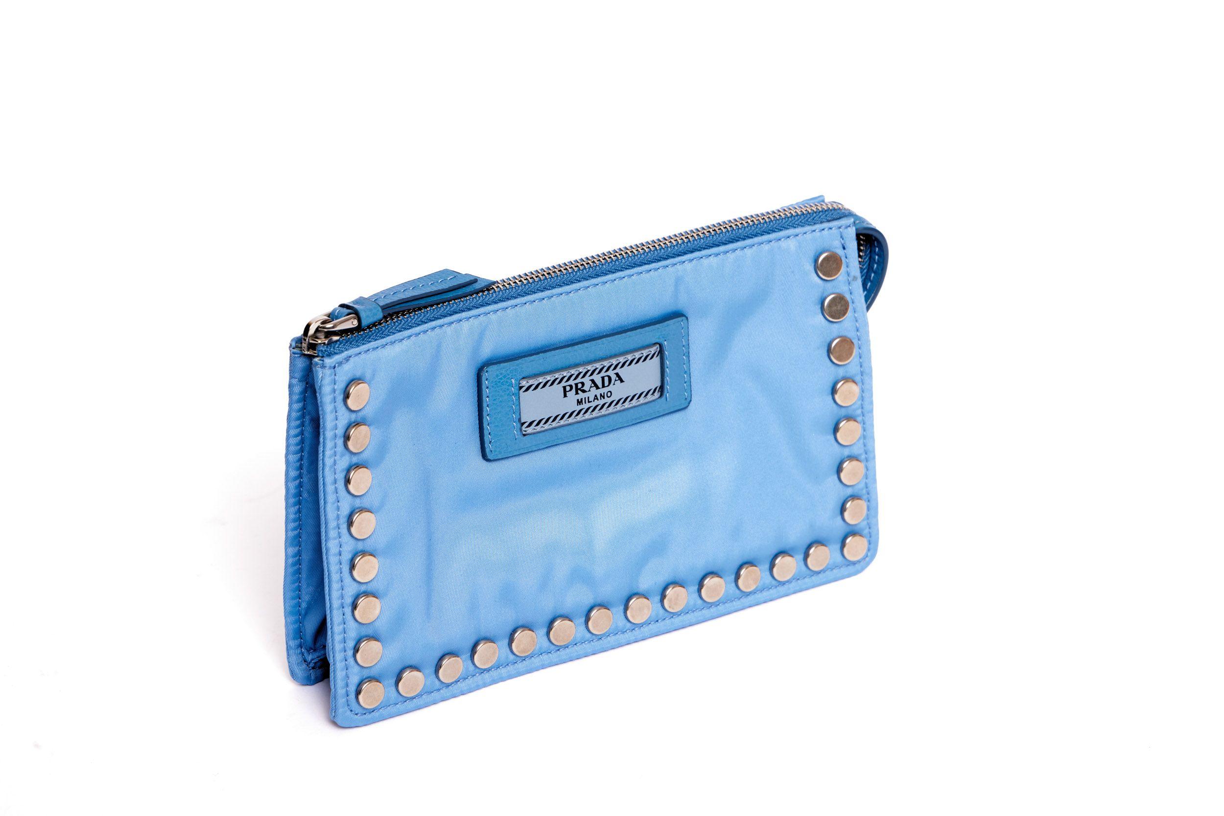 Blue fabric Prada pochette with silver metal studs and a blue leather logo tag. The hardware is in a silver-tone. The pochette is in excellent condition and comes with the authenticity card and original box.