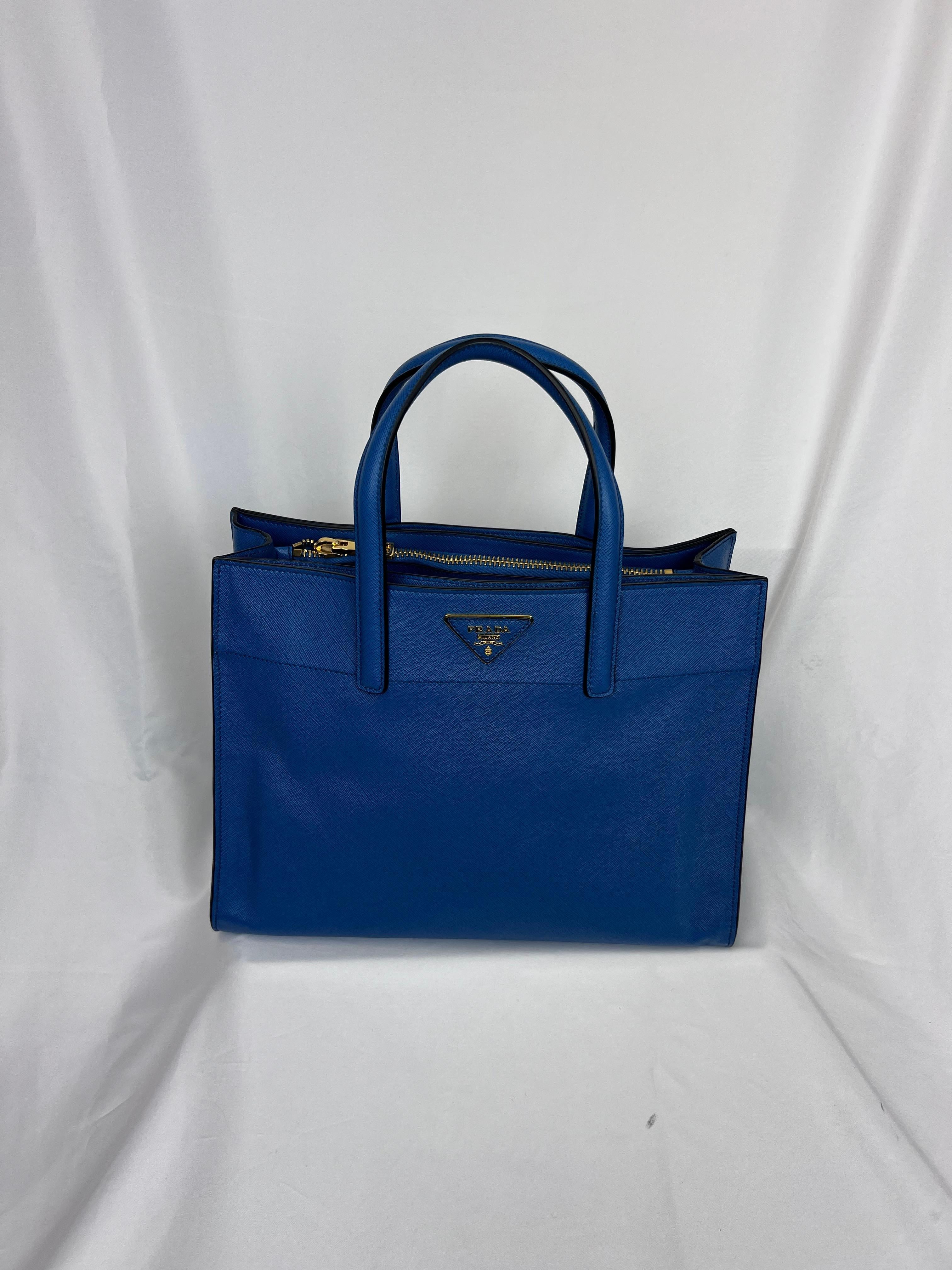 This Prada tote, crafted in iconic blue Saffiano leather, combines elegance and functionality. The structured design features three spacious pockets, including a central zip compartment, offering plenty of organized storage for daily essentials. The
