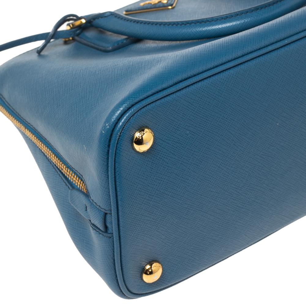 This satchel from the House of Prada brings you endless elegance along with complete essentiality. Fashioned in blue Saffiano Lux leather, this satchel has a dome-like silhouette that is accentuated with gold-toned fittings. Dual handles and a roomy