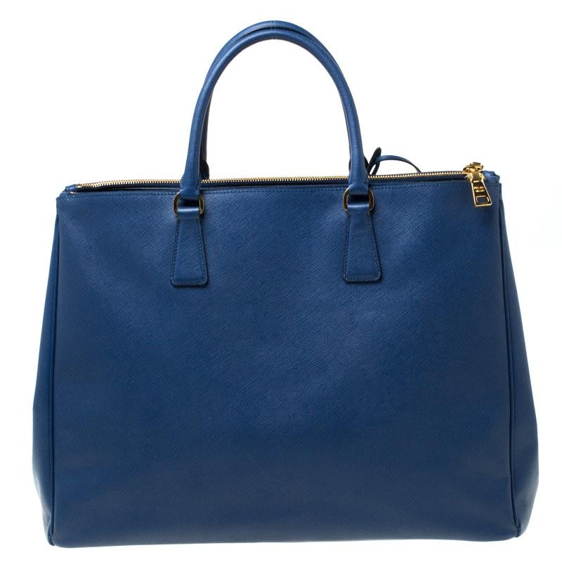 Feminine in shape and grand in design, this Double Zip tote by Prada will be a loved addition to your closet. It has been crafted from Saffiano lux leather and styled minimally with gold-tone hardware. It comes with two top handles, two zip