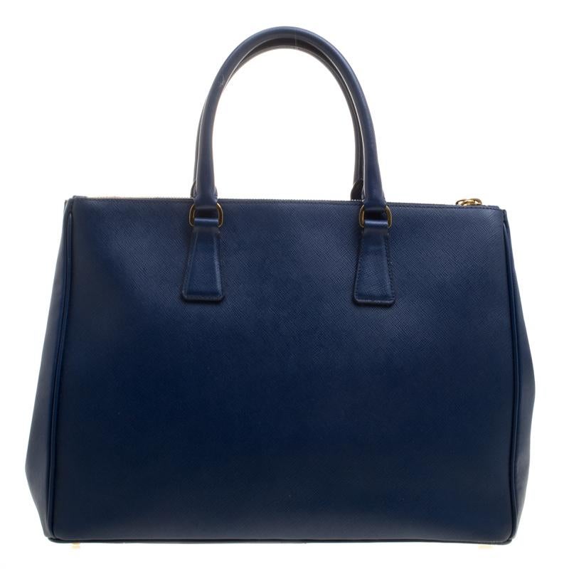 Beautifully crafted from Saffiano Lux leather, this Prada tote is a creation you can't miss. It has a classy blue exterior along with two zippers and a spacious nylon interior that will hold your necessities. The bag is held by two handles, and