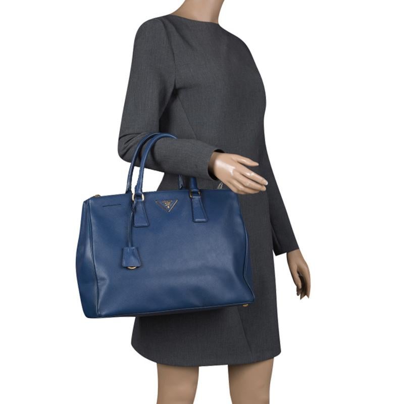 Beautifully crafted from Saffiano Lux leather, this Prada tote is a creation you can't miss. It has a classy blue exterior along with two zippers and a spacious nylon interior that will hold your necessities. The bag is held by two handles, and